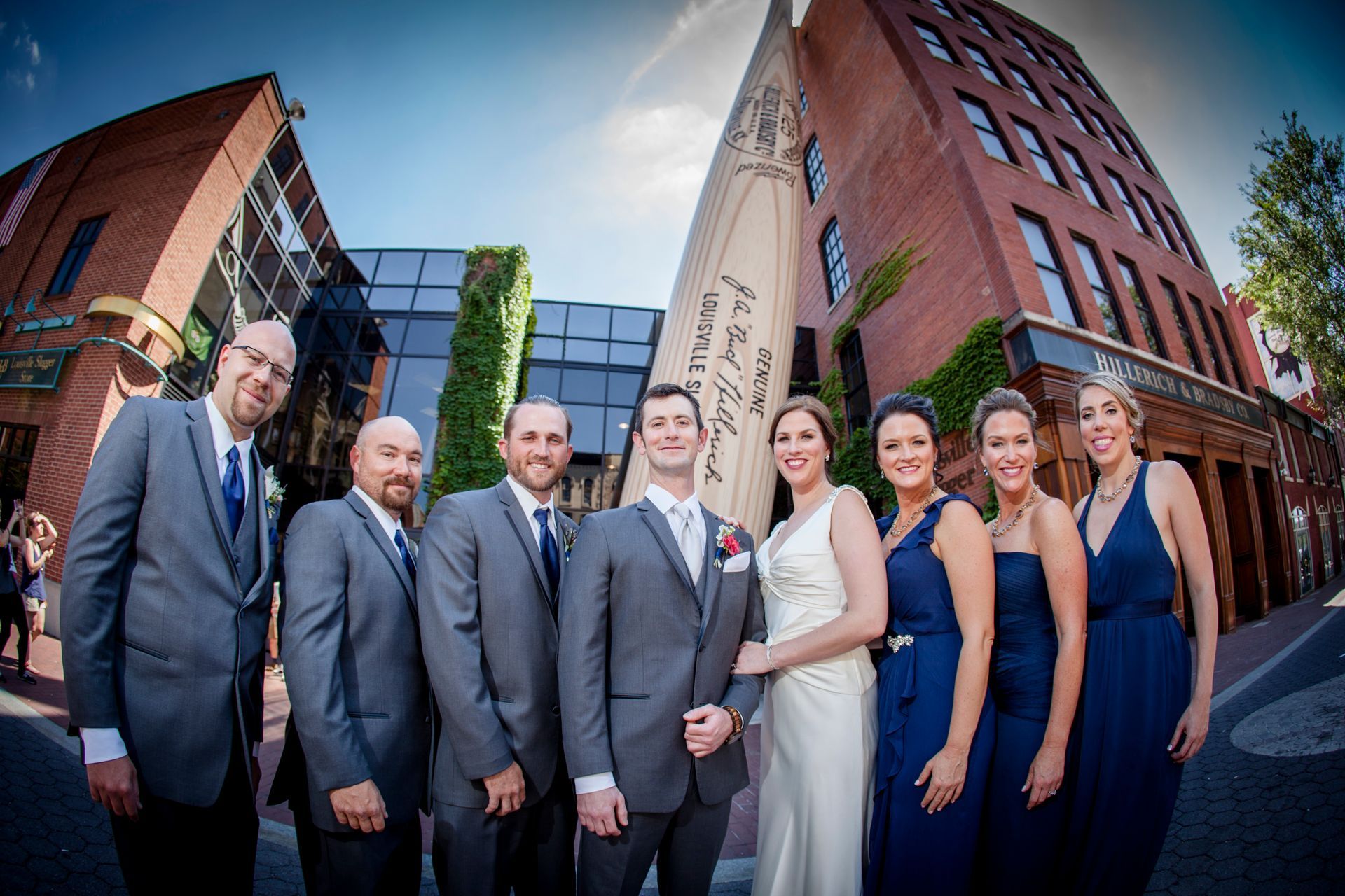 Group in formal attire posing outdoors between red-brick buildings with a clear blue sky