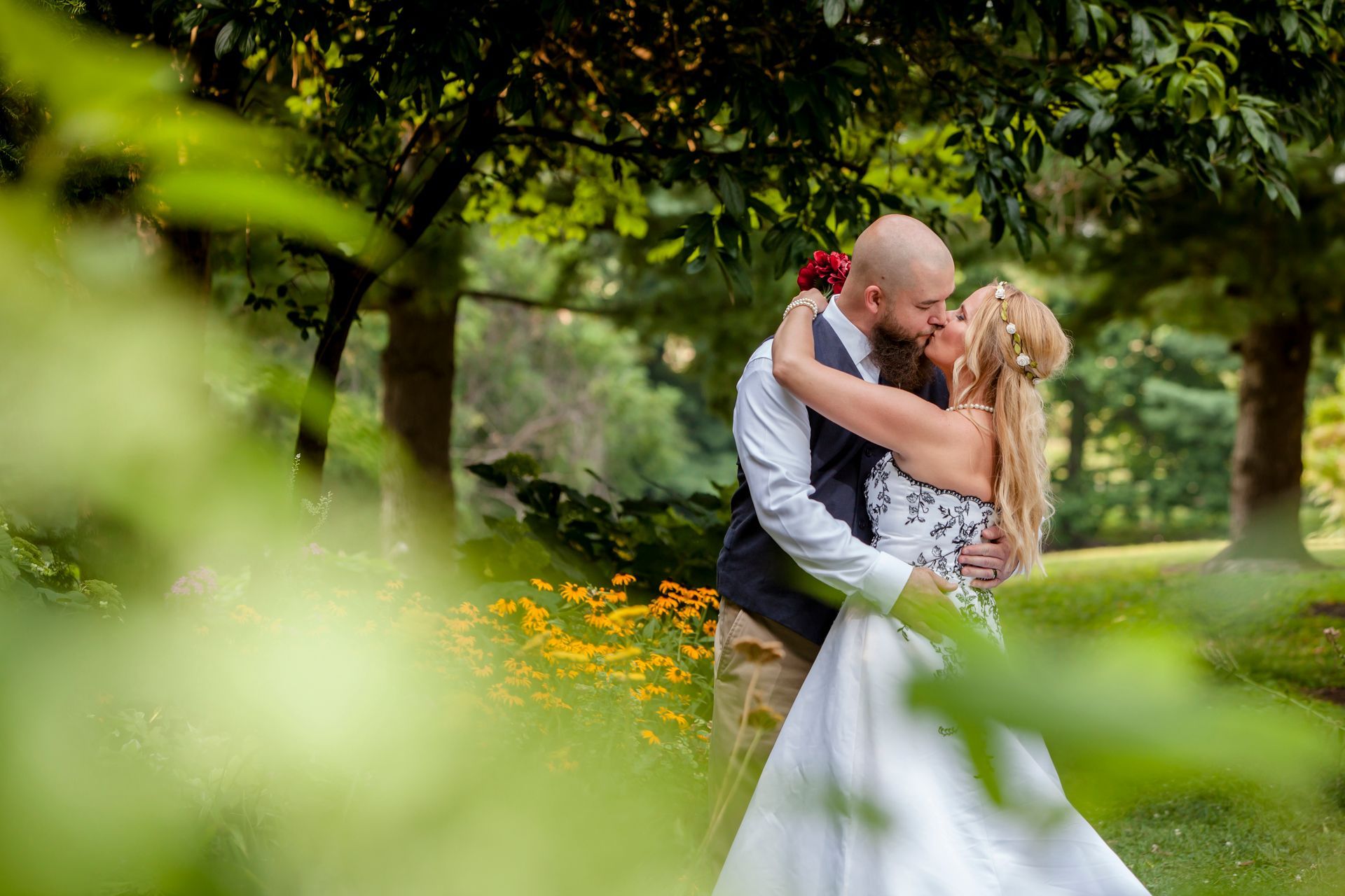 Couple embracing in a garden, with green foliage and yellow flowers framing the scene.