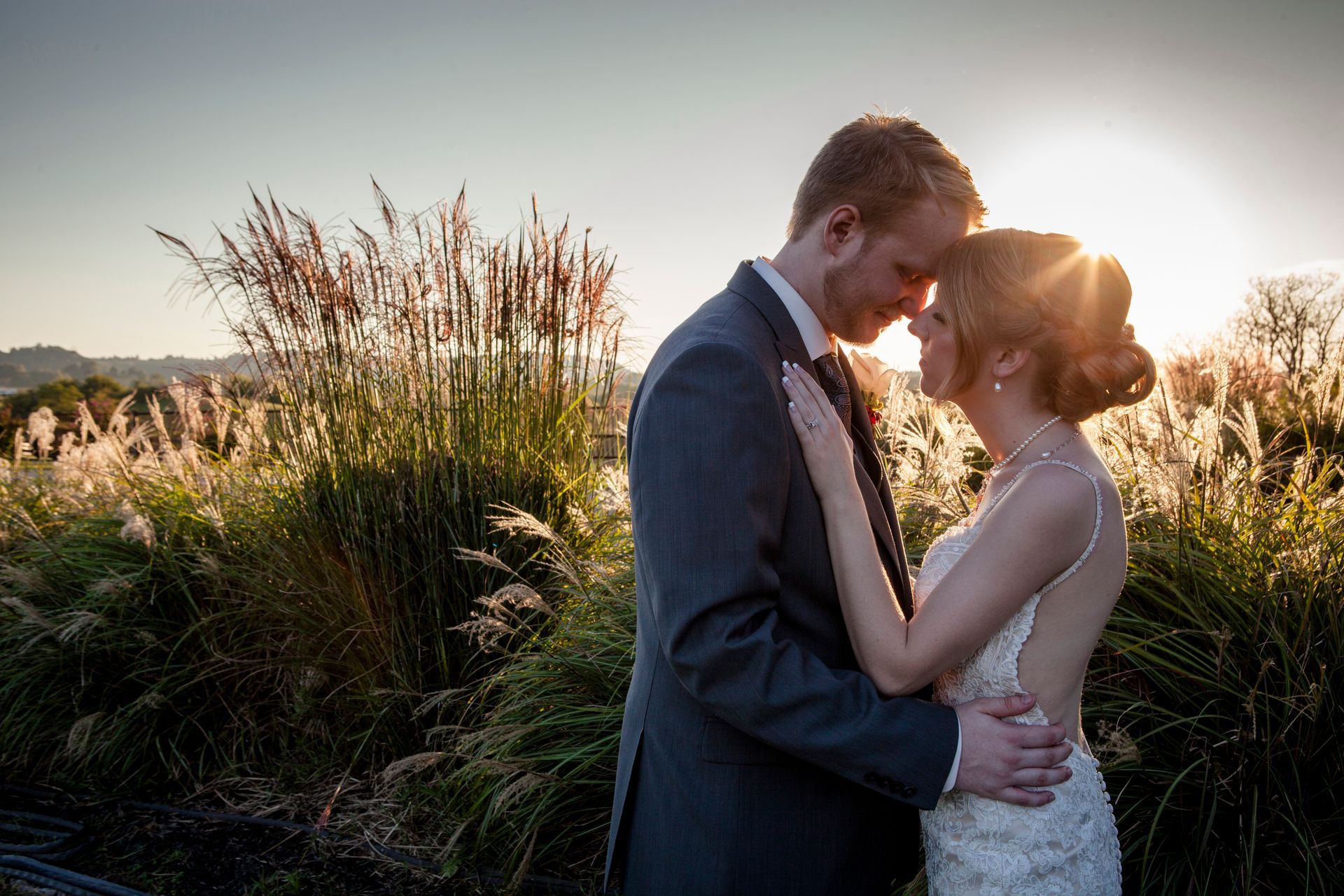 Couple embracing and kissing at sunset in a grassy field, backlit by warm golden light