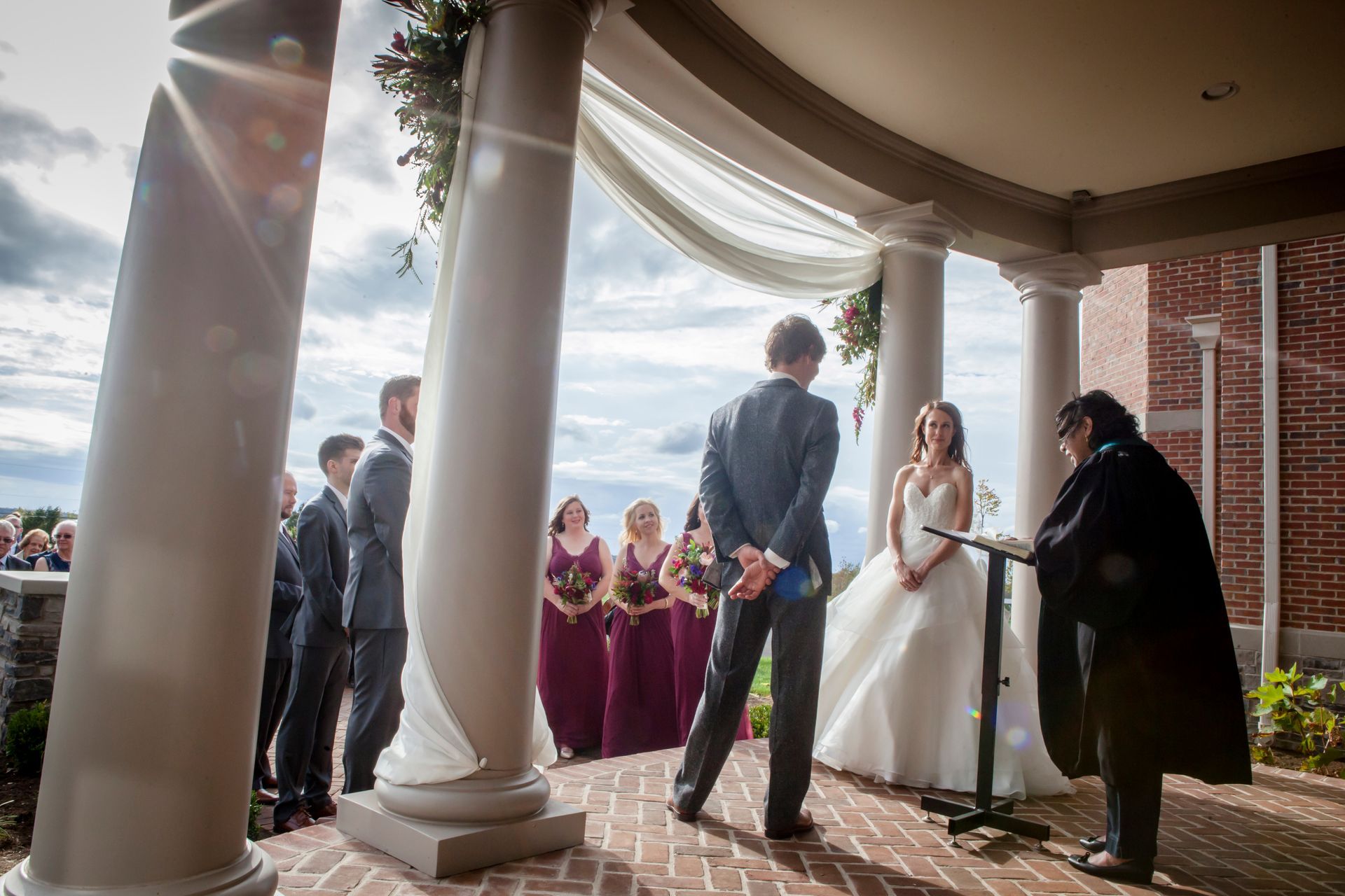 Outdoor wedding ceremony under a white pavilion, bride and groom at the altar with guests nearby