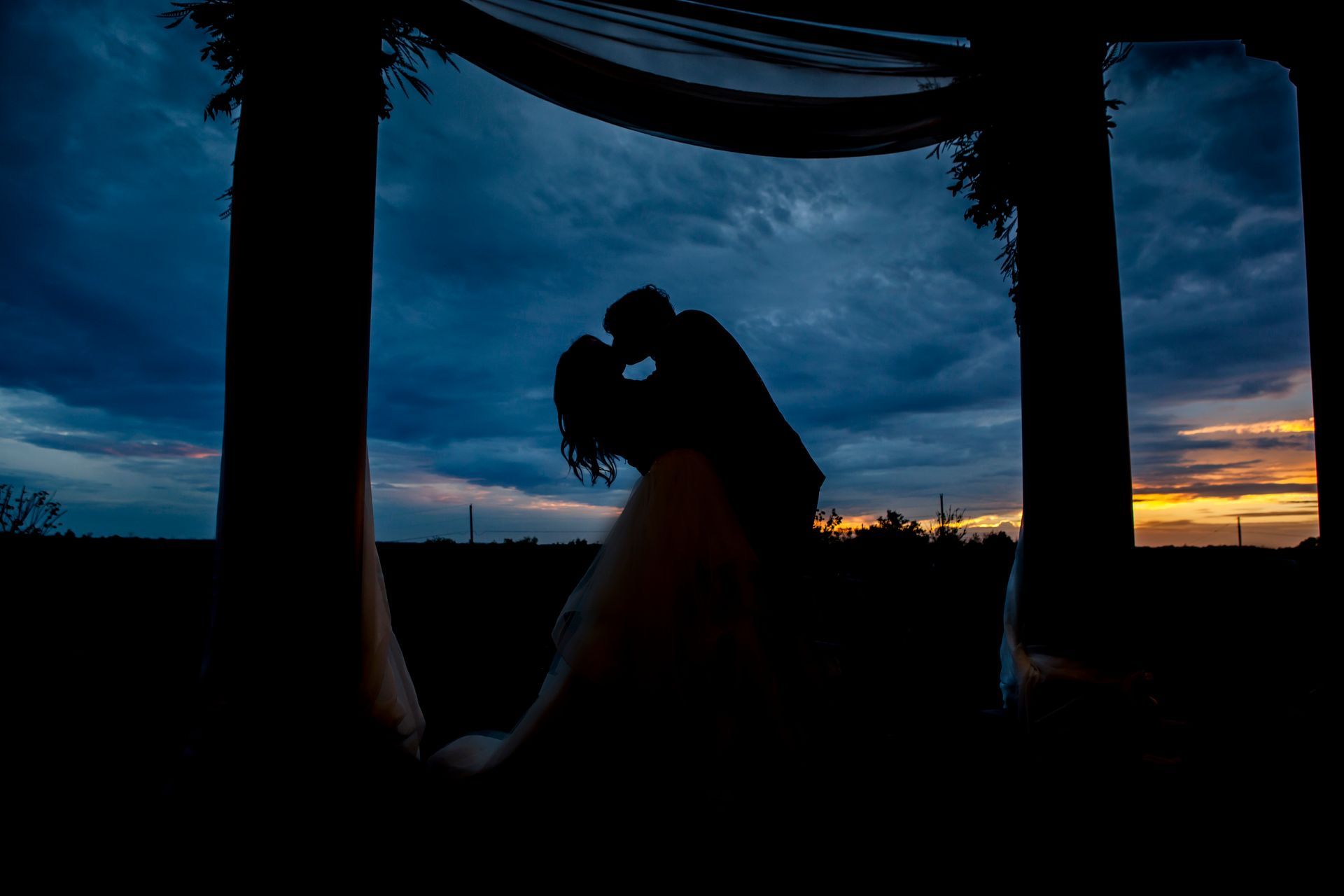 Silhouette of a couple embracing under a pavilion at sunset with a blue-orange sky