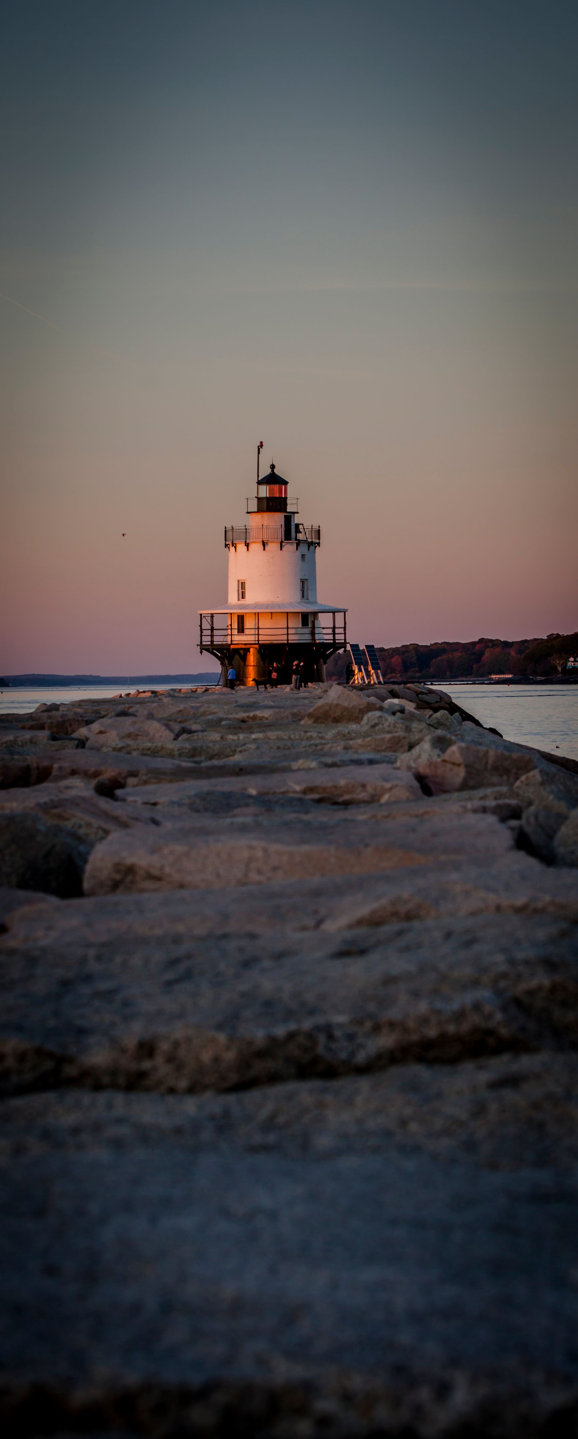 Lighthouse at dusk on a rocky shoreline with a soft pastel sky