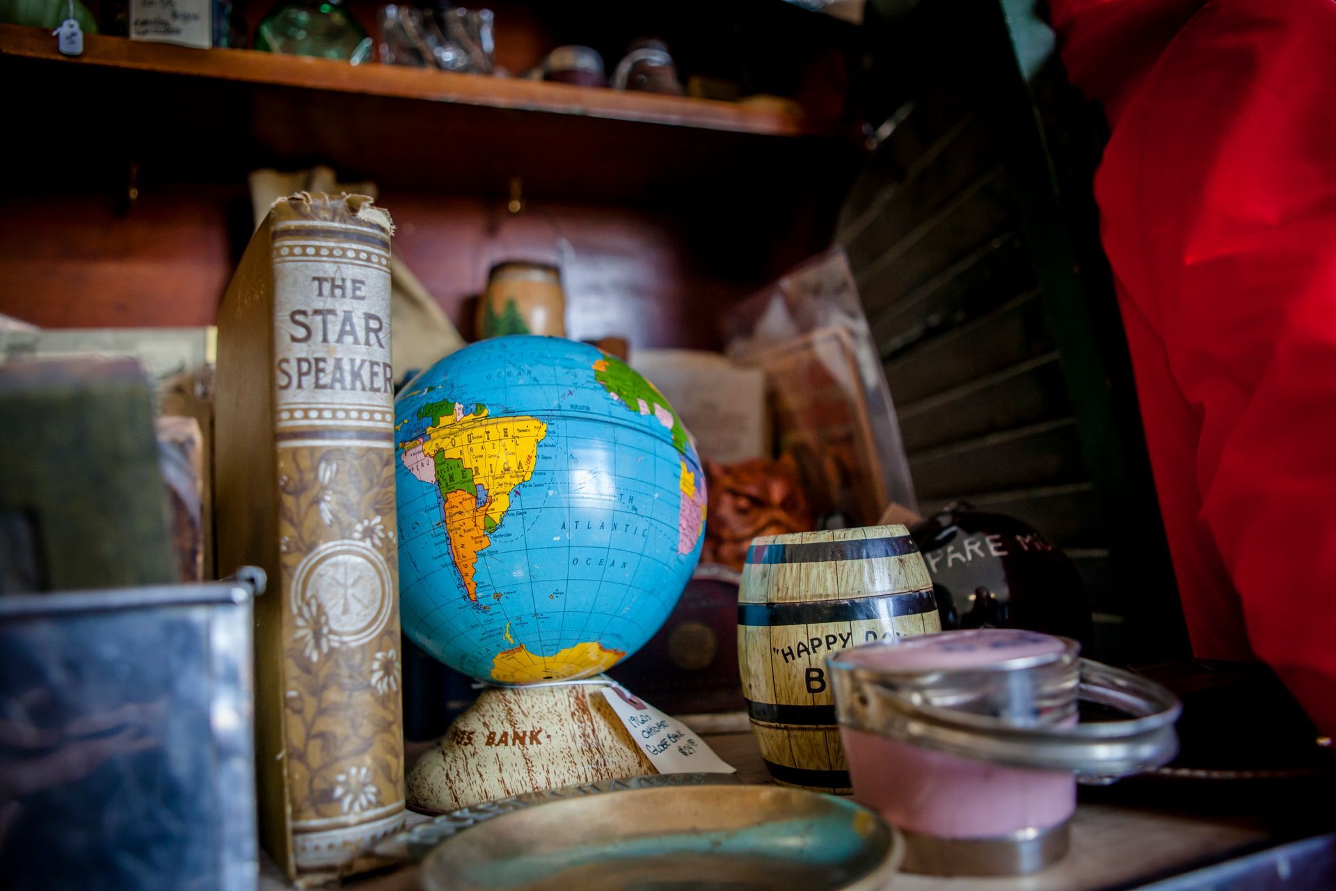 Small globe beside books, jars, and a candle on a wooden shelf in warm light.
