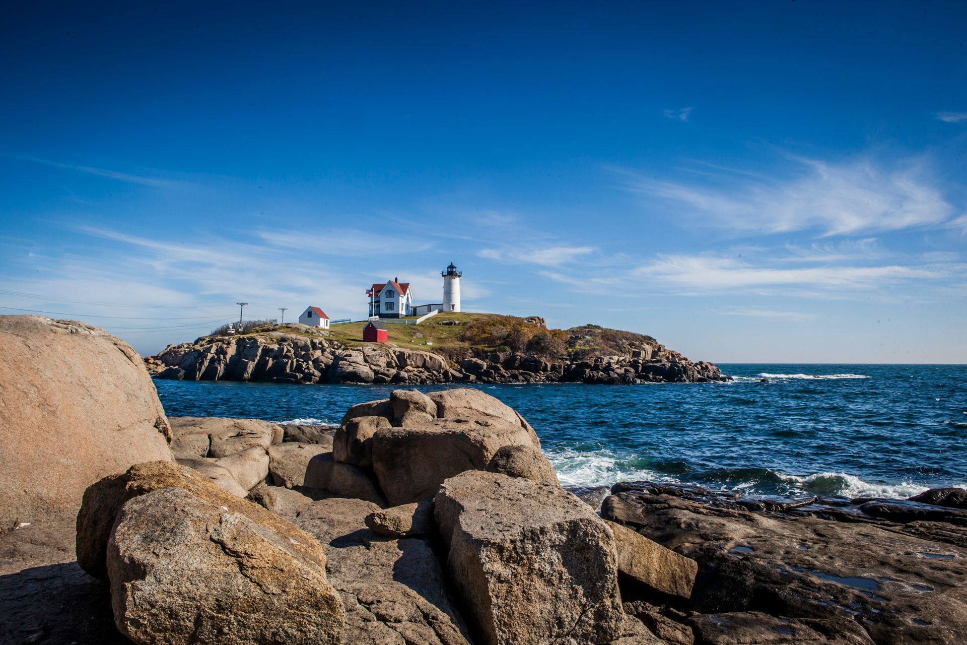 Rocky shoreline with a lighthouse on a small island under a bright blue sky