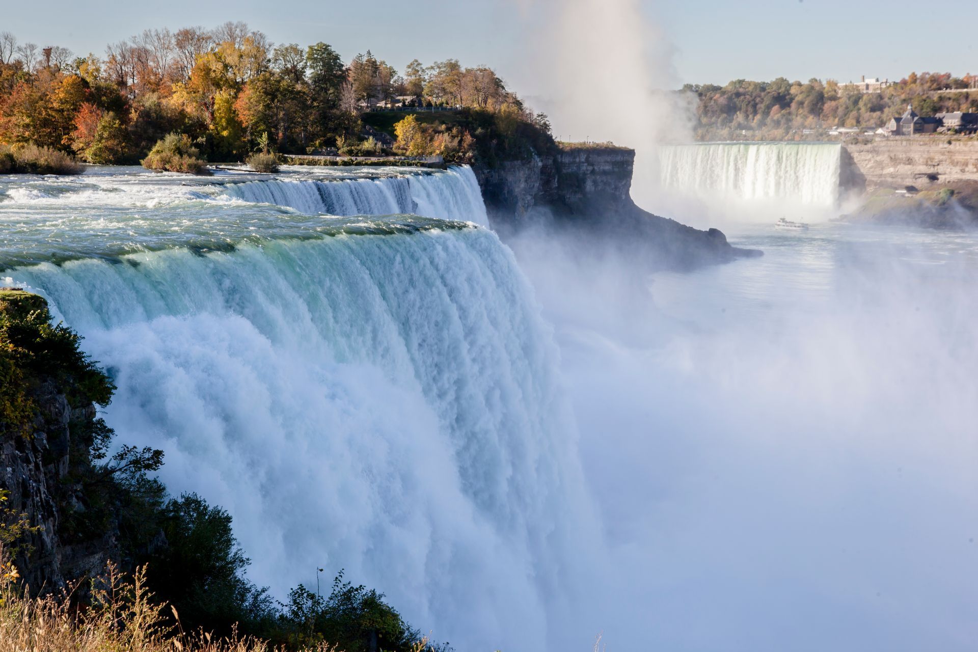Large waterfalls cascading over cliffs with mist rising and autumn trees along the rim