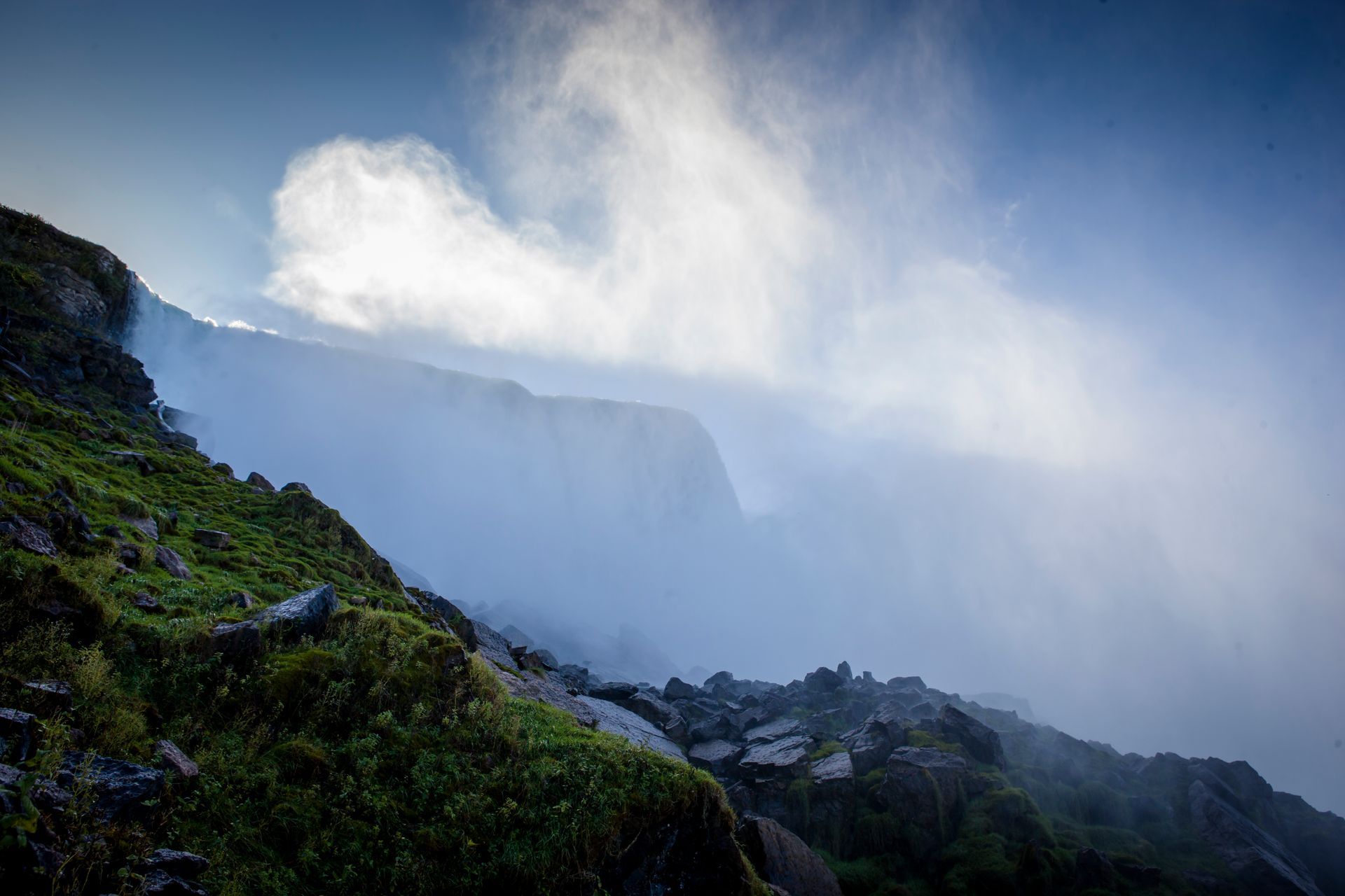Misty waterfall cascading over cliffs beside a green rocky hillside