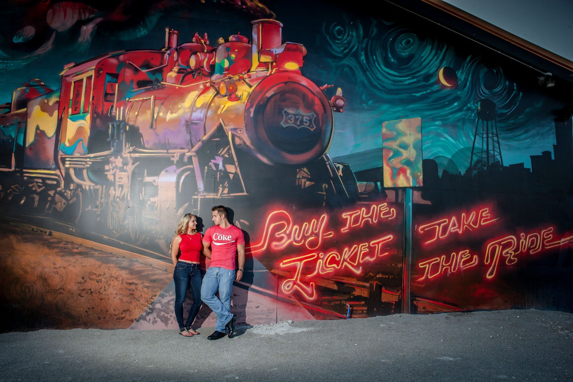 Two people stand before a colorful train mural with neon graffiti and swirling dark-blue background.