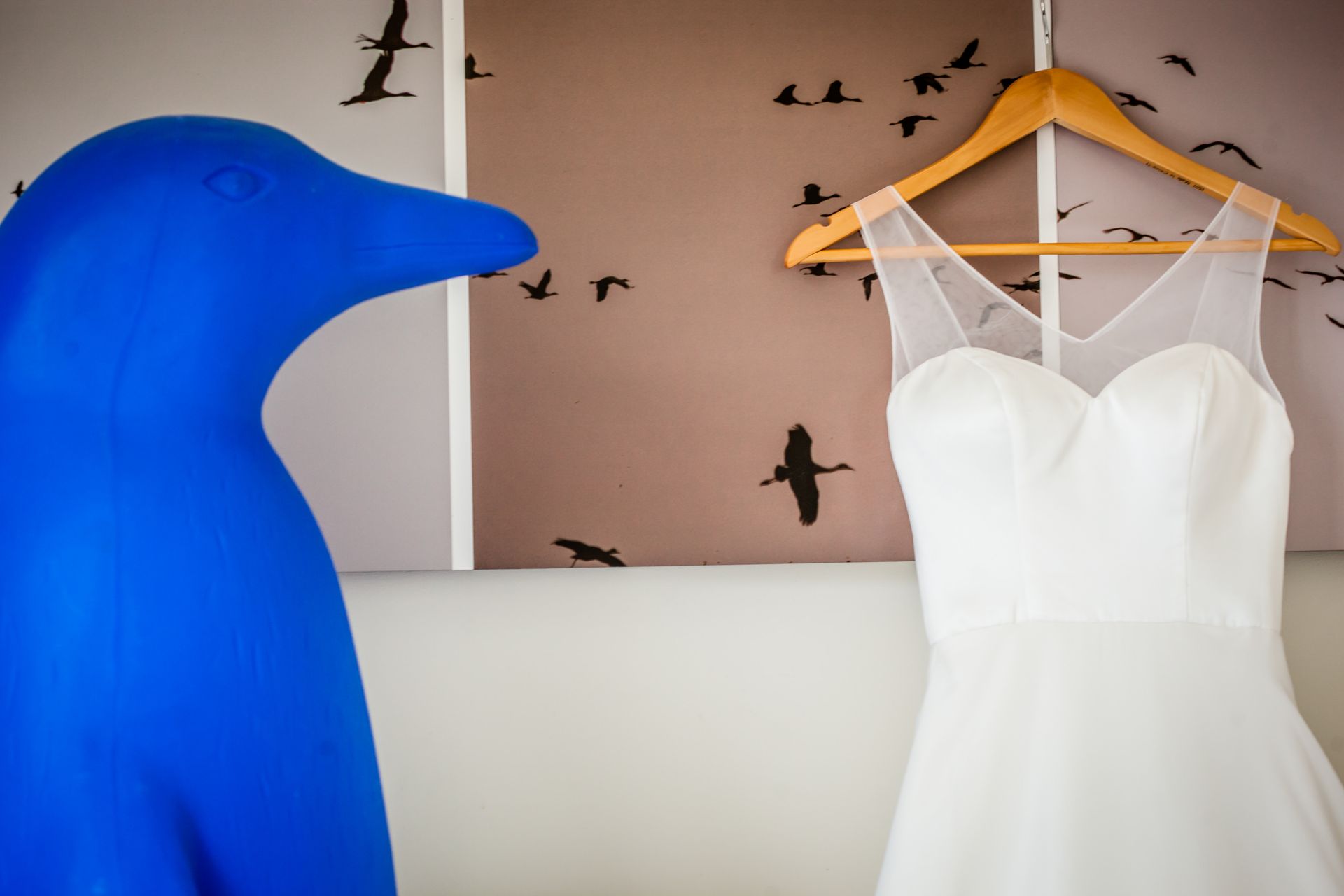 White dress on hanger beside blue bird sculpture and bird-patterned wall art