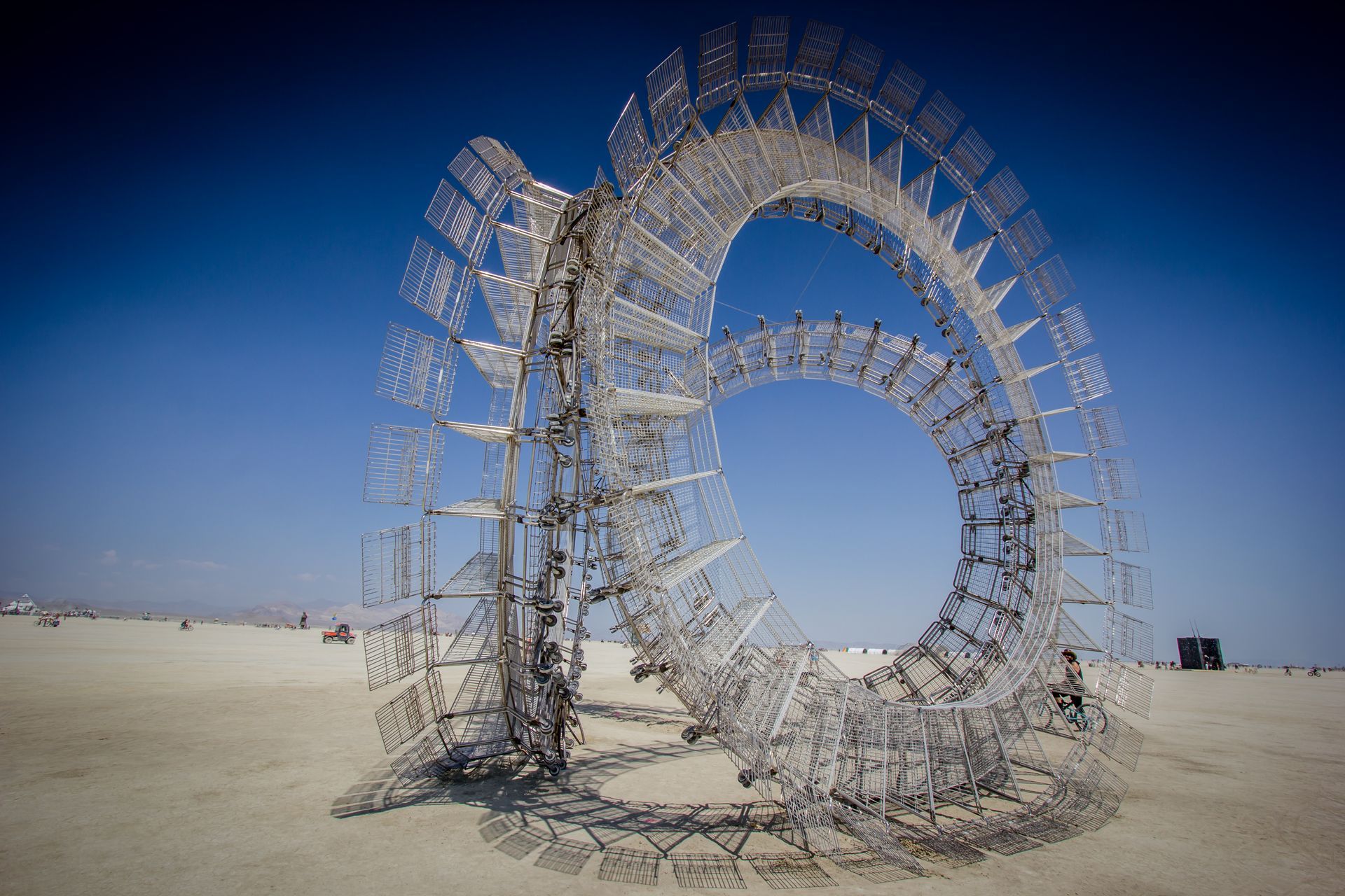 Large circular metal sculpture on a sandy desert plain under a clear blue sky
