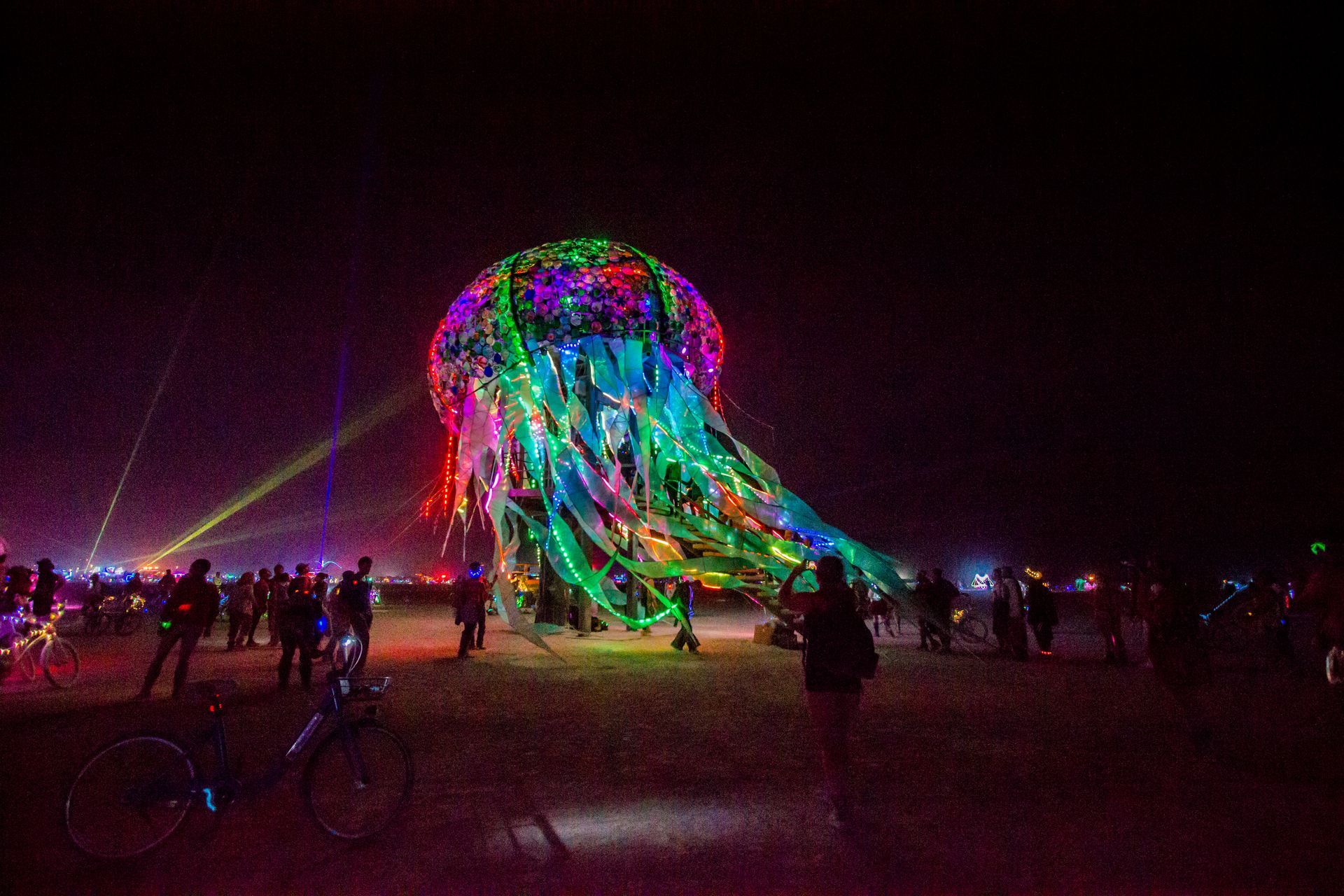 Nighttime festival with a giant glowing jellyfish light sculpture and people watching nearby