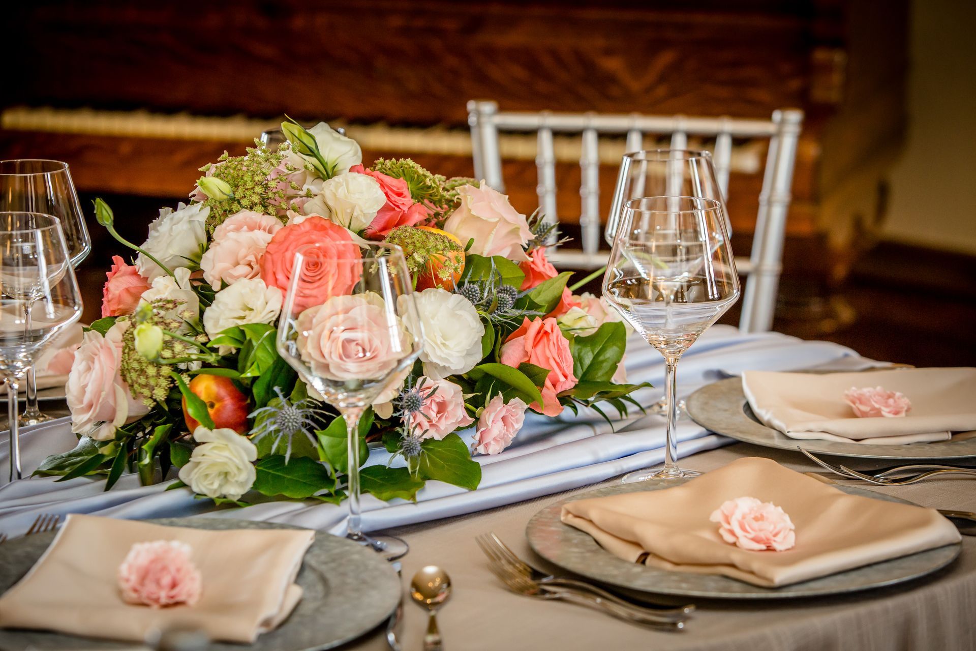 Elegant wedding reception table with pink floral centerpiece, candles, glassware, and beige napkins