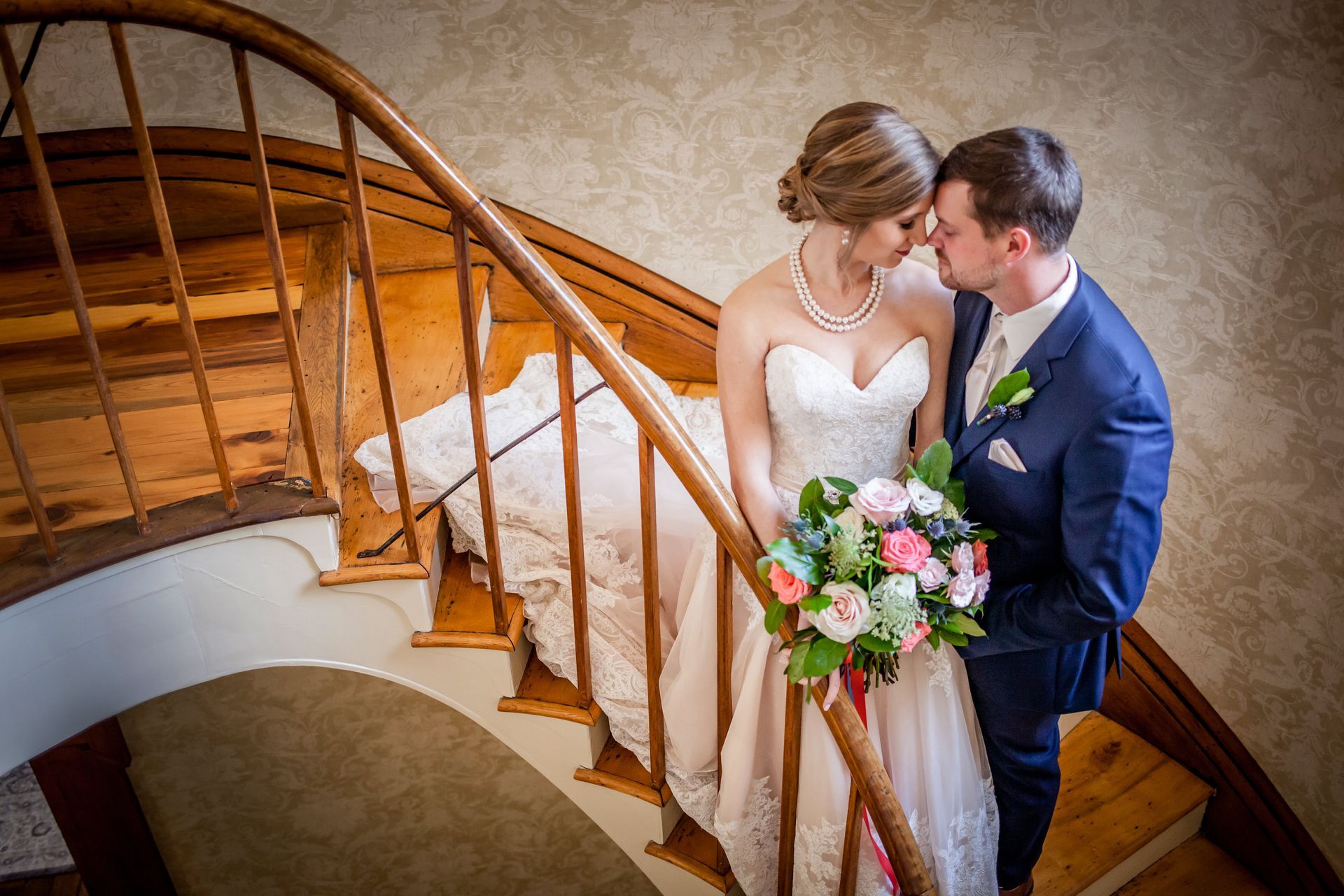 Bride and groom kissing on a wooden staircase, the bride holding a bouquet of pink and white flowers.