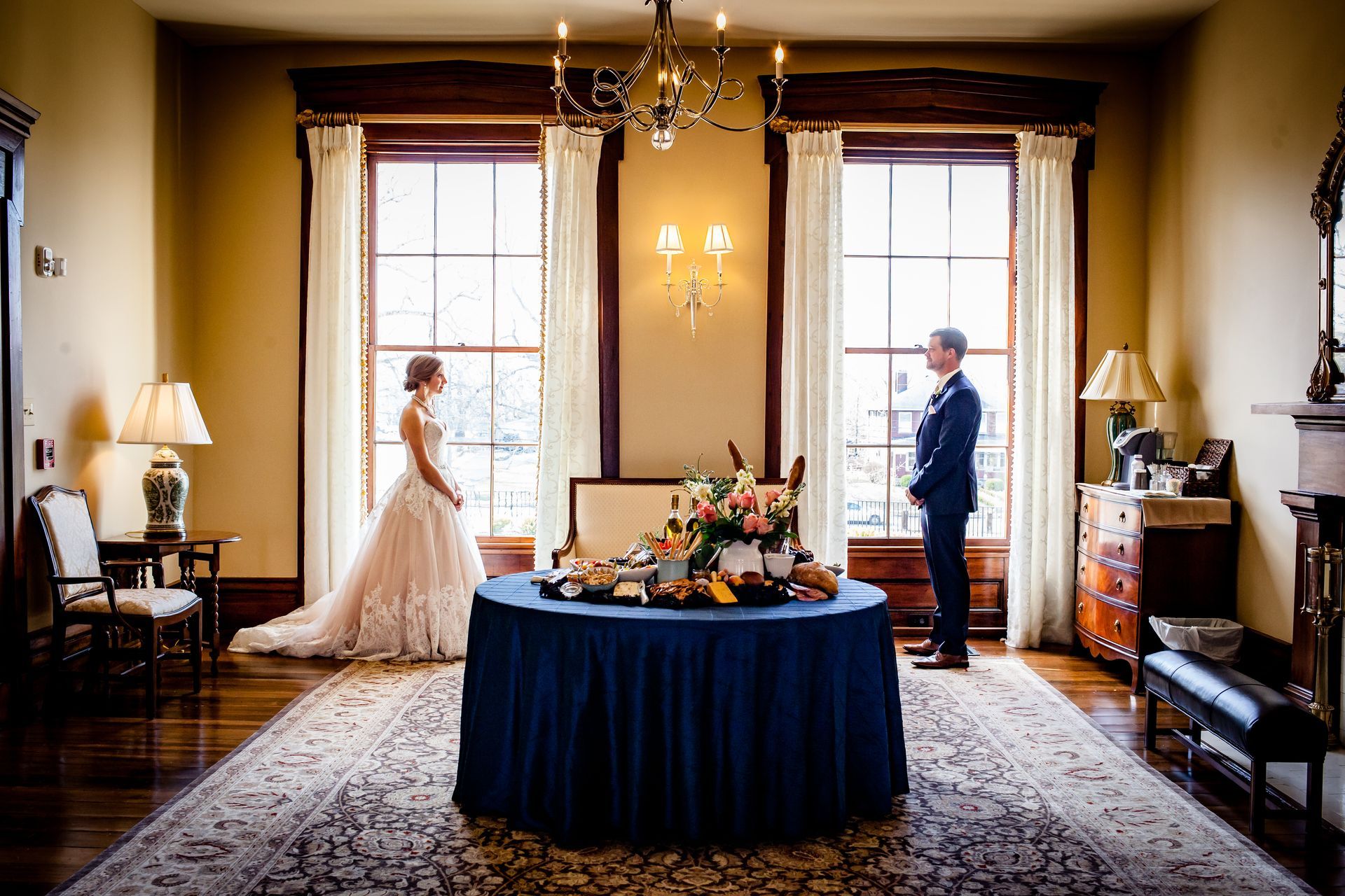 Bride and groom standing apart in a warmly lit formal dining room with a table centerpiece बीच