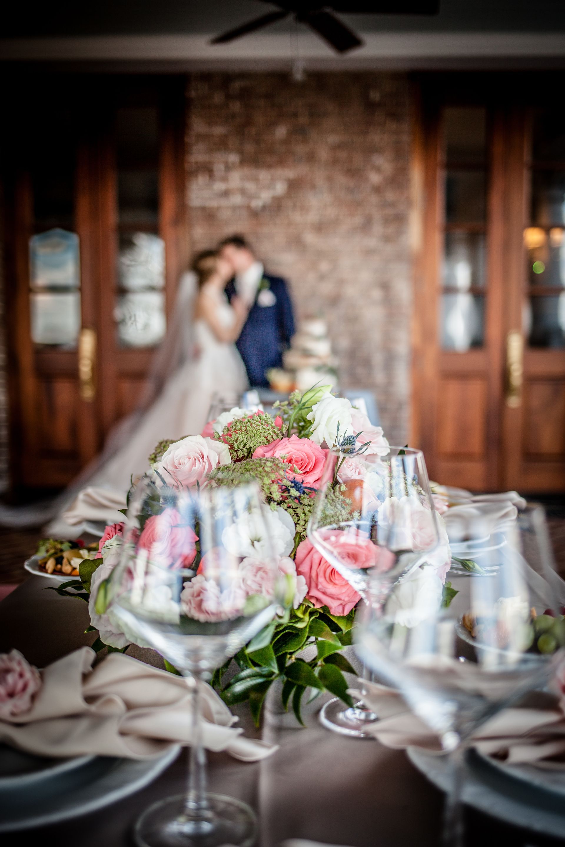 Wedding couple embracing behind a flowered table, with blurred champagne glasses in the foreground.