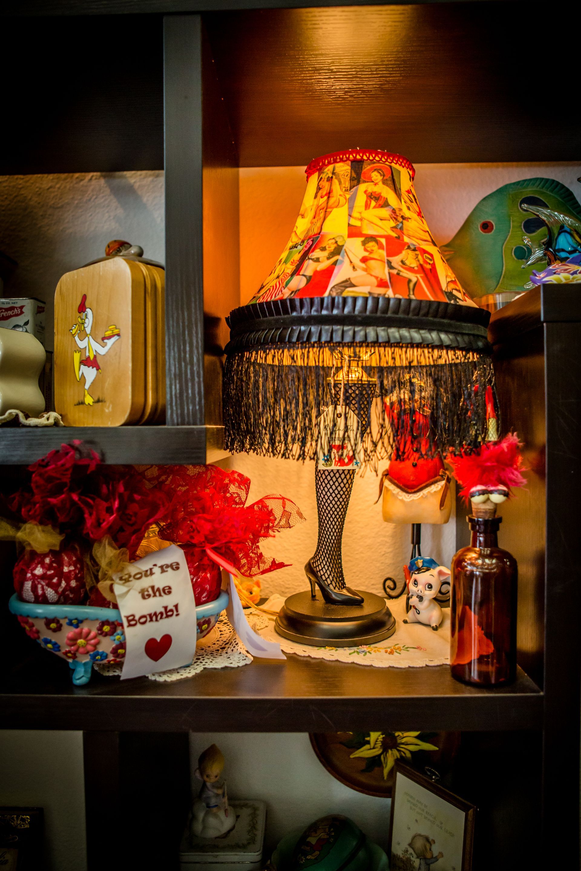 Shelf of decorative lamps and vases, featuring a fringed table lamp with a colorful floral shade.