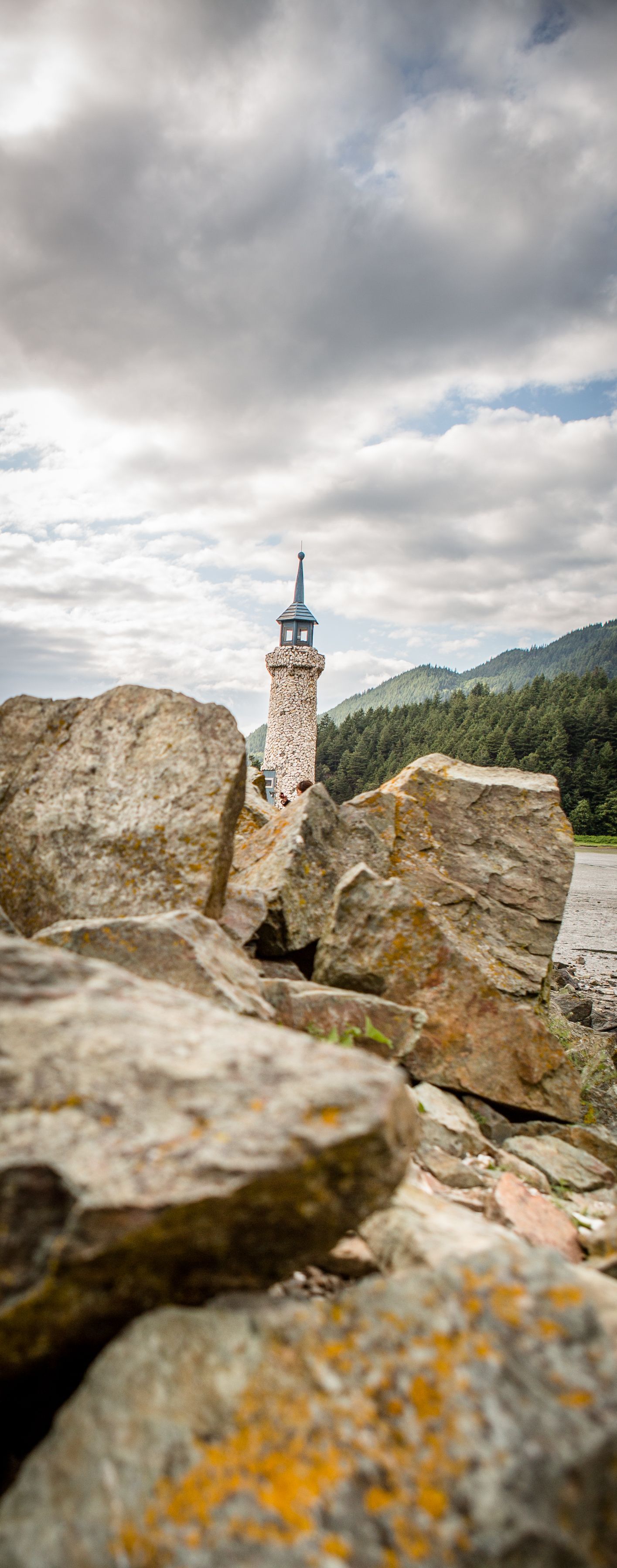 Rocky foreground with a tall stone spire under cloudy mountains and sky.