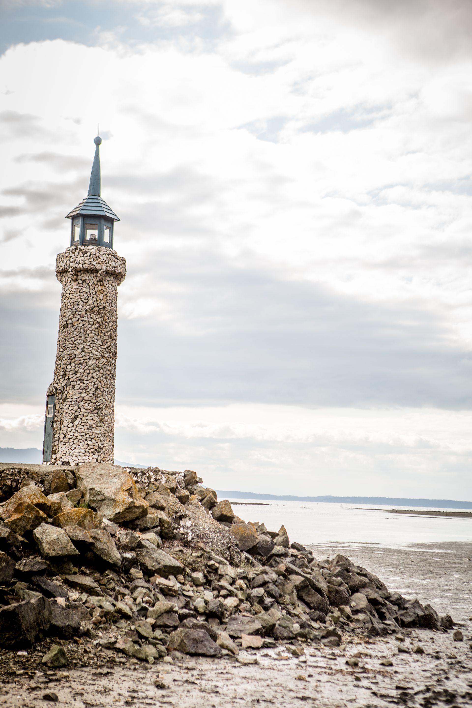 Stone lighthouse on a rocky shoreline beside calm water under a cloudy sky