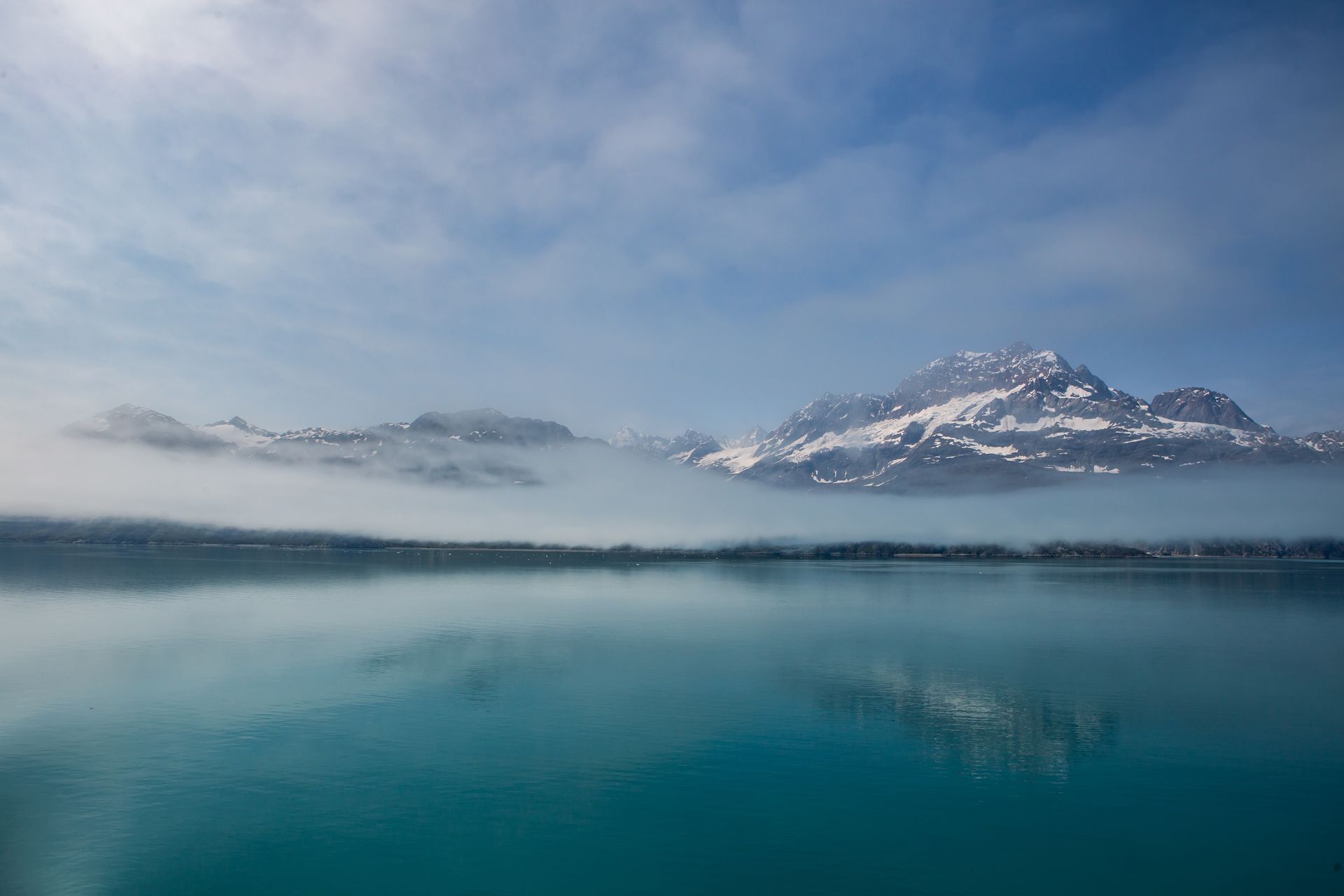 Snowy mountain reflected in a calm blue lake under a misty sky