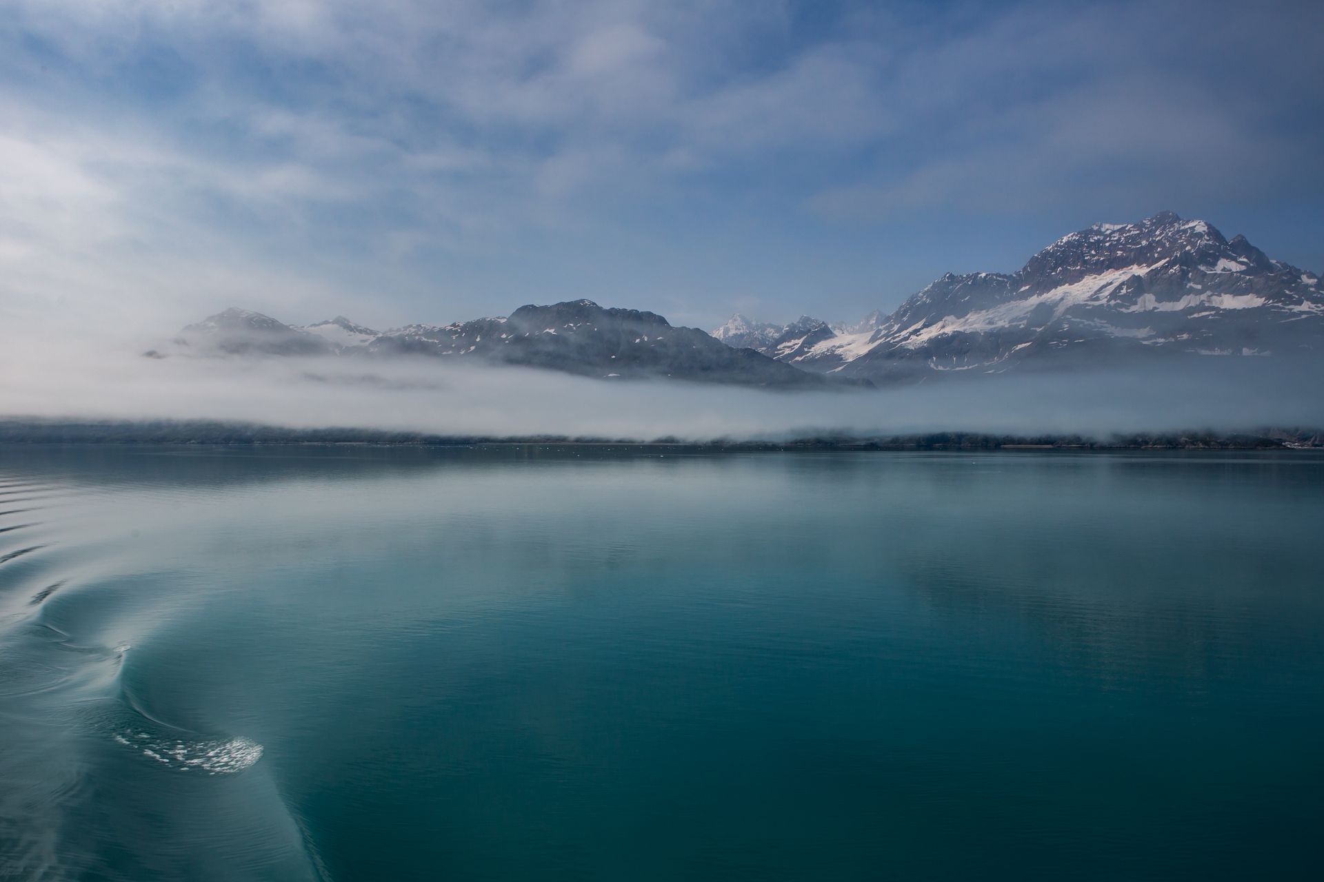 Snowy mountains reflected in a calm blue lake under a cloudy sky