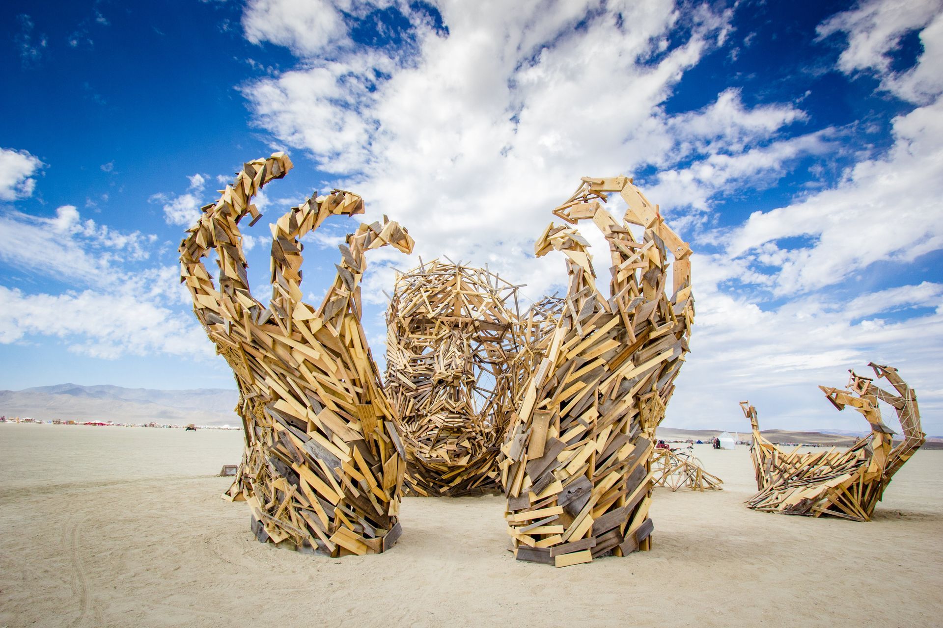 Dramatic wood sculptures shaped like raised hands in a desert under a bright blue sky with clouds