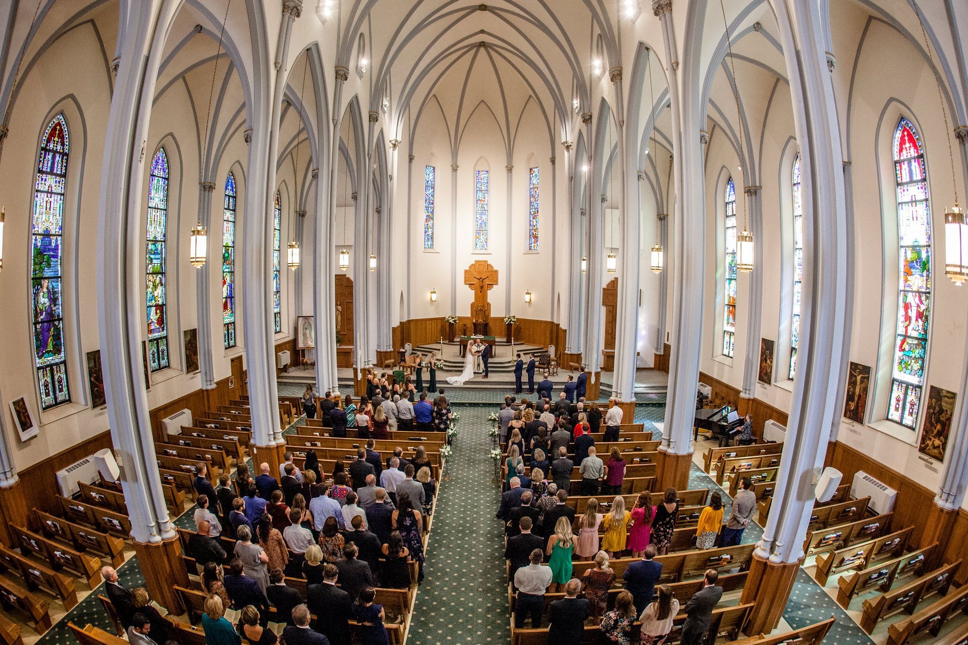 Crowded cathedral interior with people seated in pews beneath tall arches and stained-glass windows