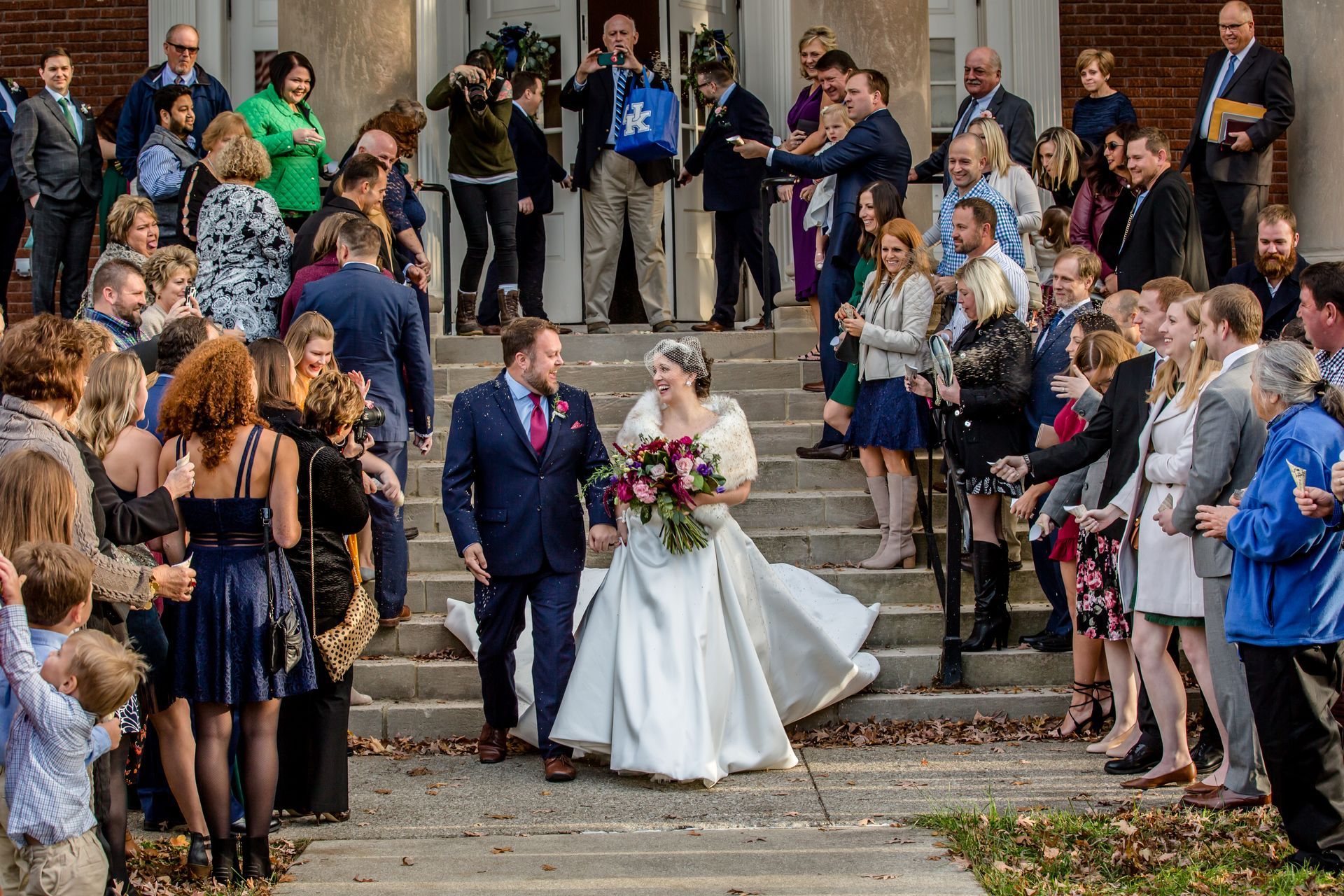 Bride and groom walking down steps through a crowd of applauding guests outdoors
