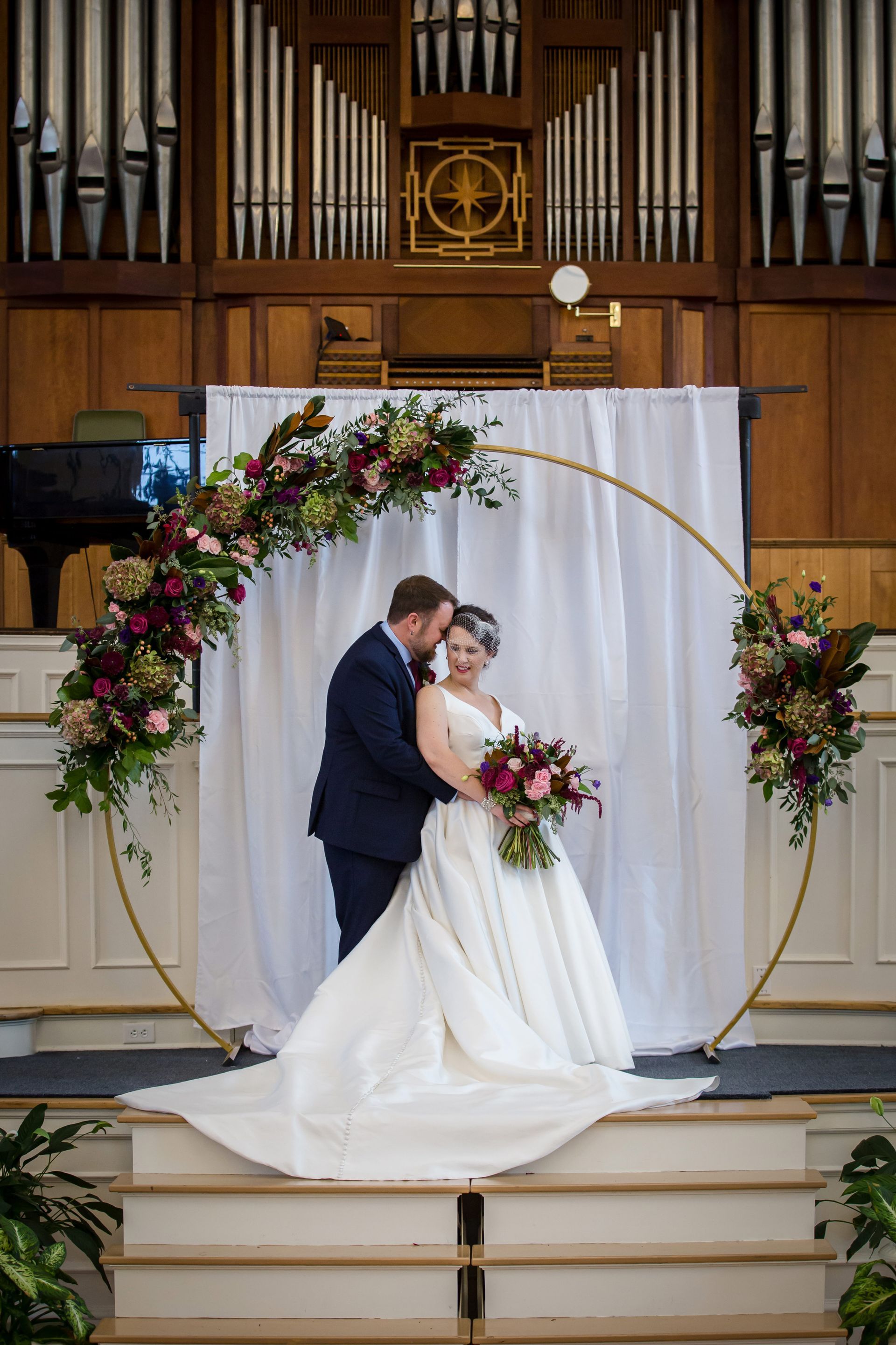 Bride and groom sharing a kiss under a floral arch on a church altar