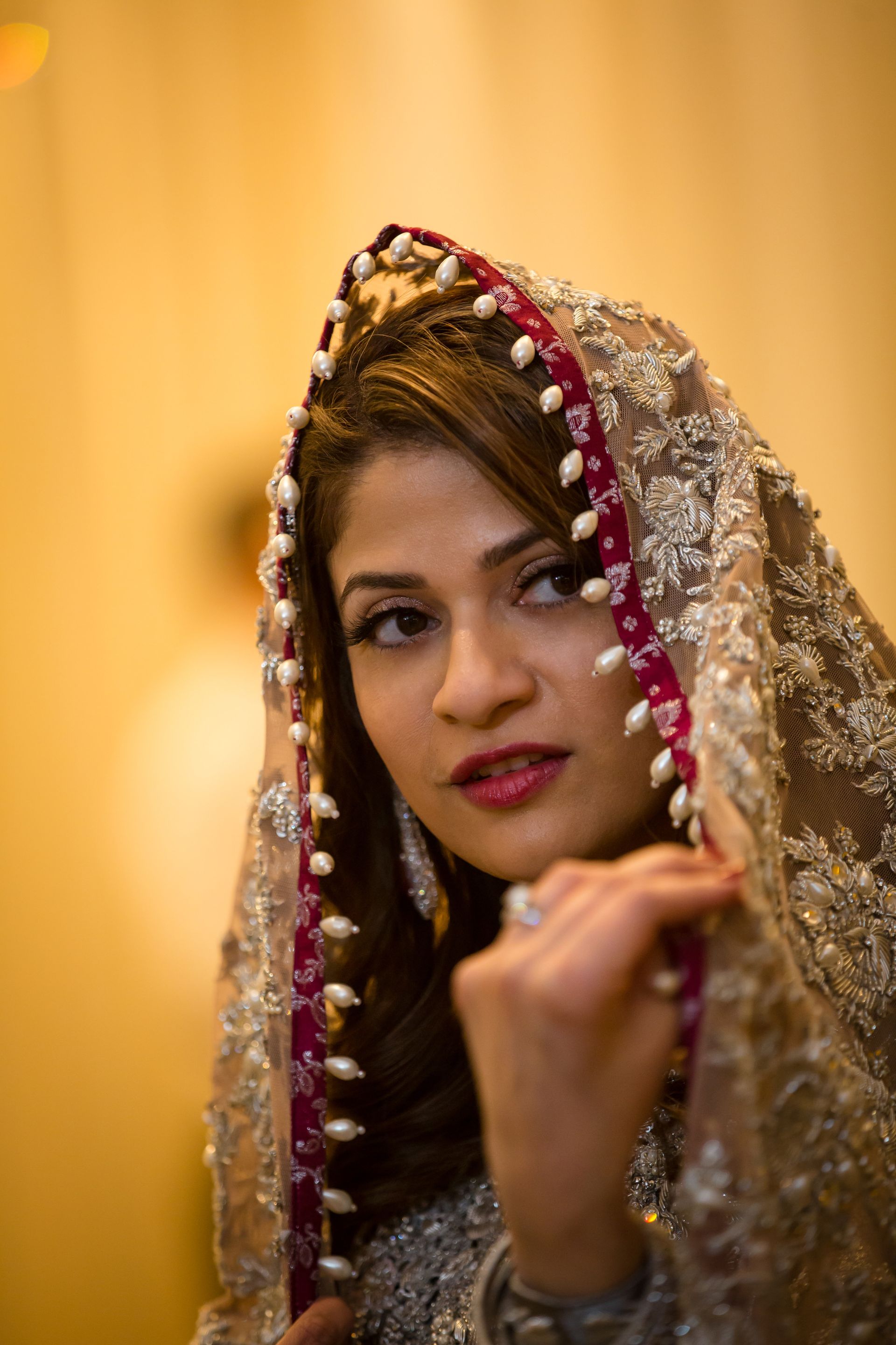 Woman in a gold embroidered veil with red trim, looking at the camera against a warm background