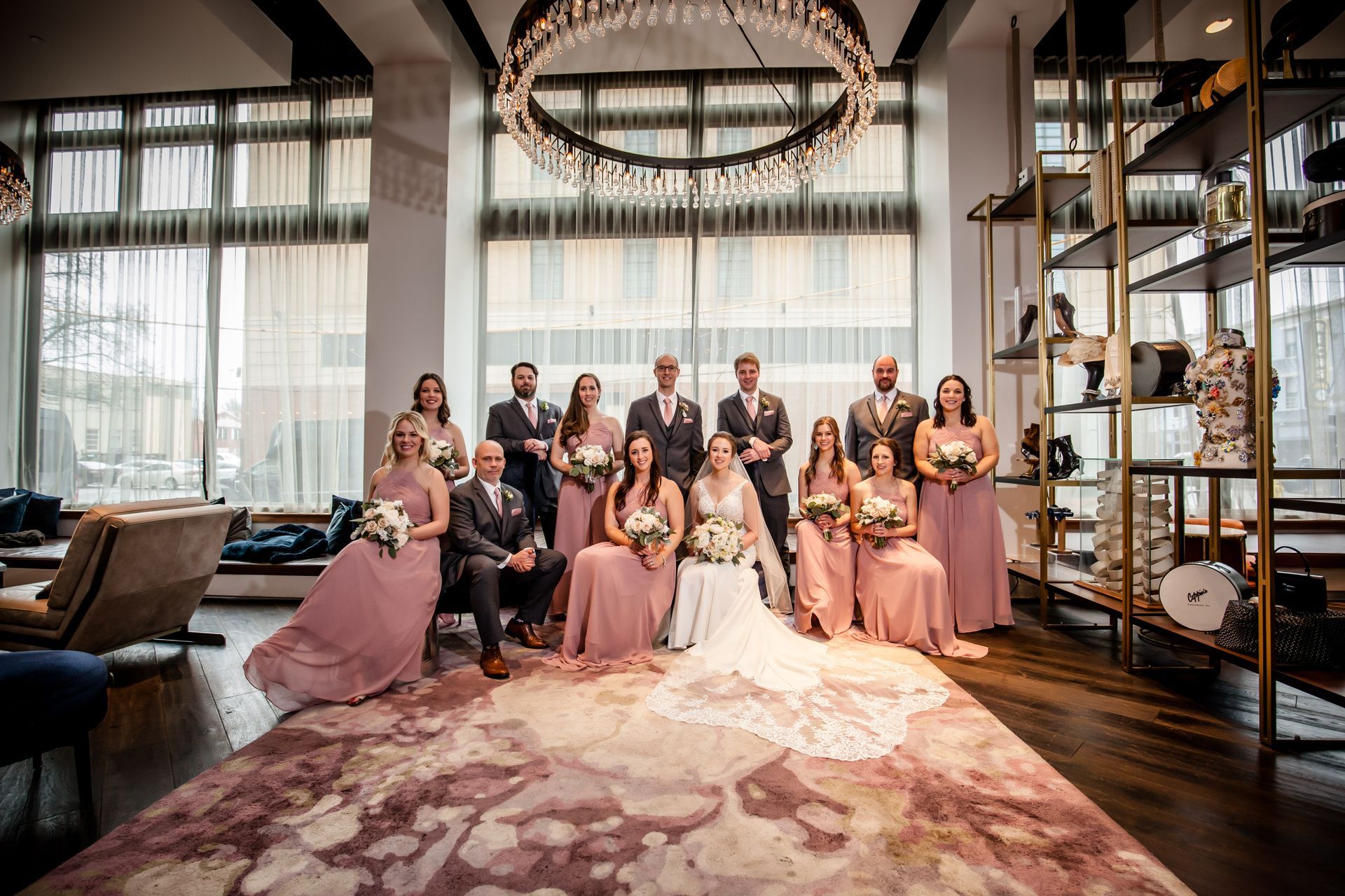 Wedding party posing in a modern lounge, with pink dresses and a long train in the foreground.
