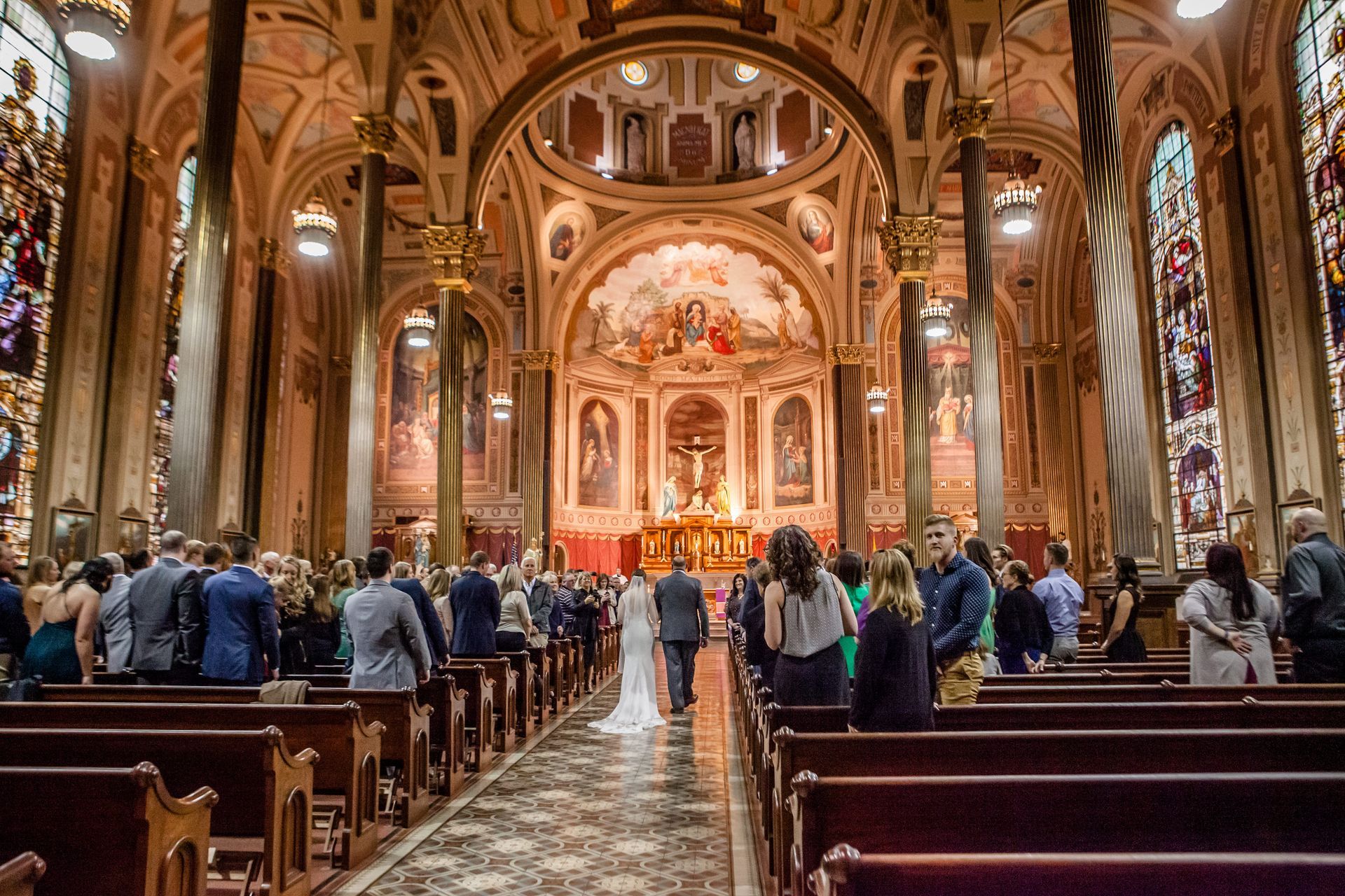 Congregants seated in a ornate church interior during a service, with a decorated altar at the front.