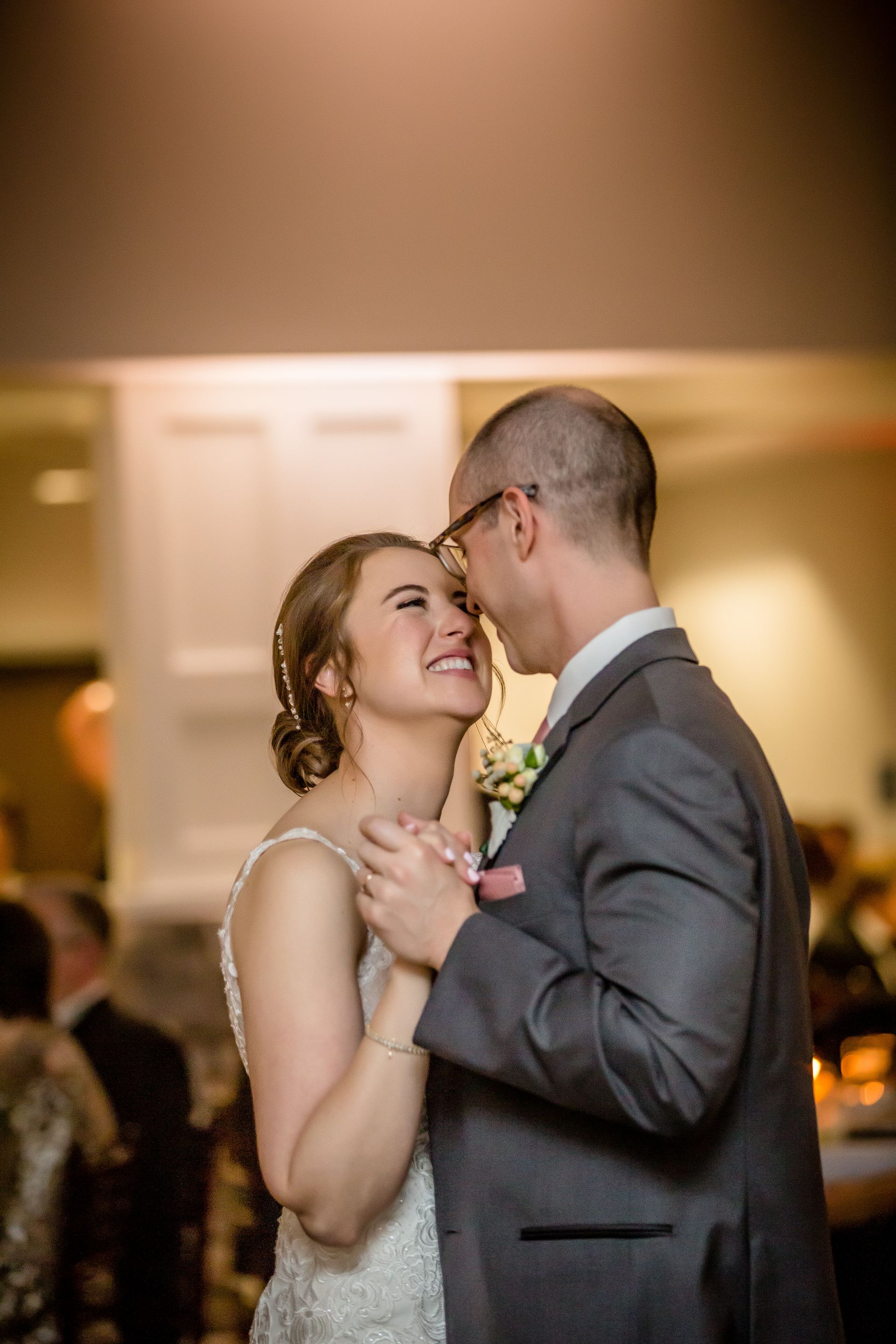 Couple in formal attire sharing a tender dance at a warmly lit reception.