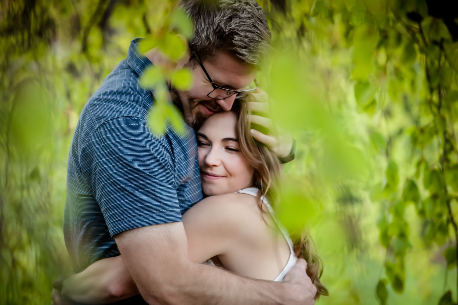 Couple embracing under green tree branches, smiling and holding each other closely
