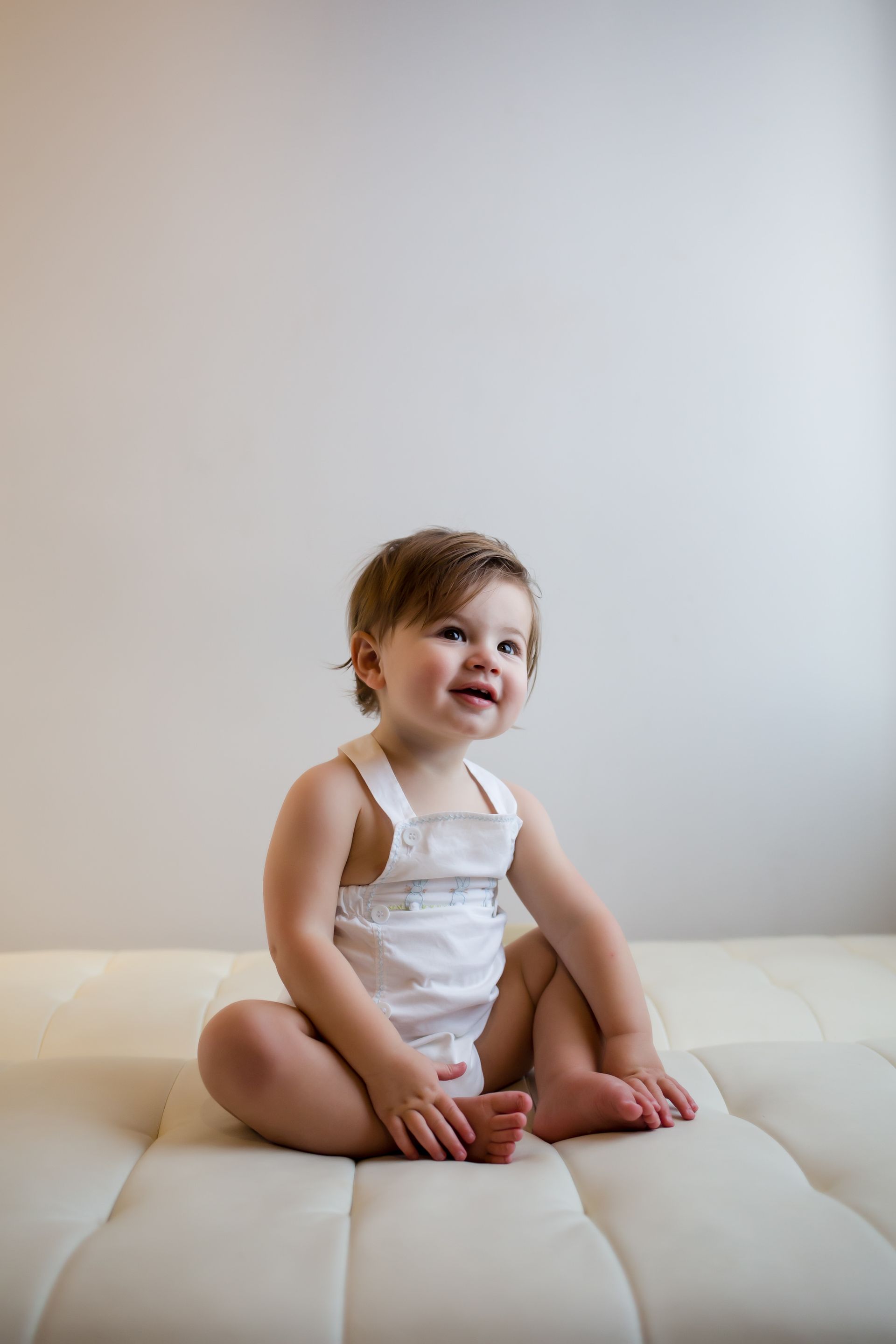 Smiling toddler sitting on a white cushion in a light, minimal room