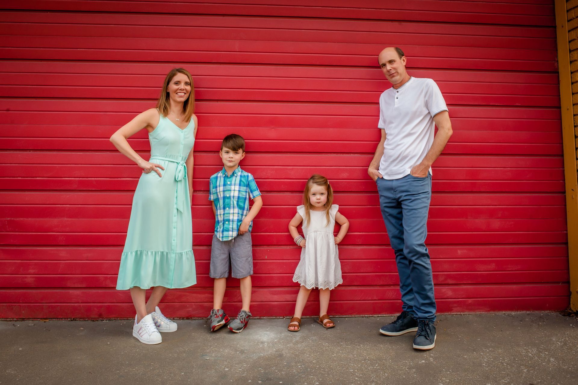 Family of four standing against a bright red wooden wall outdoors