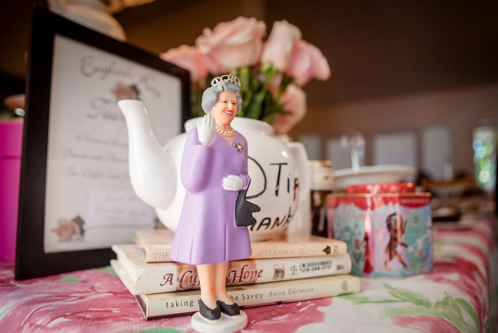 Figurine in a lavender dress on stacked books, with floral decor and framed art in the background.