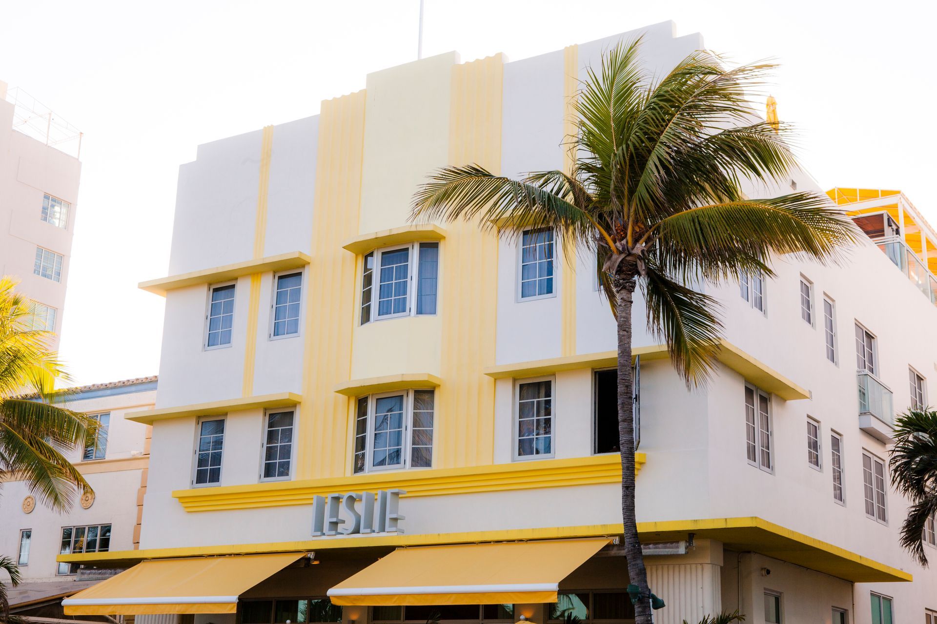 Yellow-and-white apartment building with palm trees in front and awnings at street level
