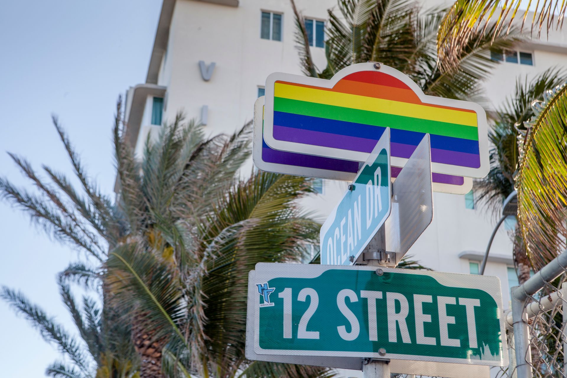 Rainbow pride sign above “12 STREET” sign near palm trees and a building