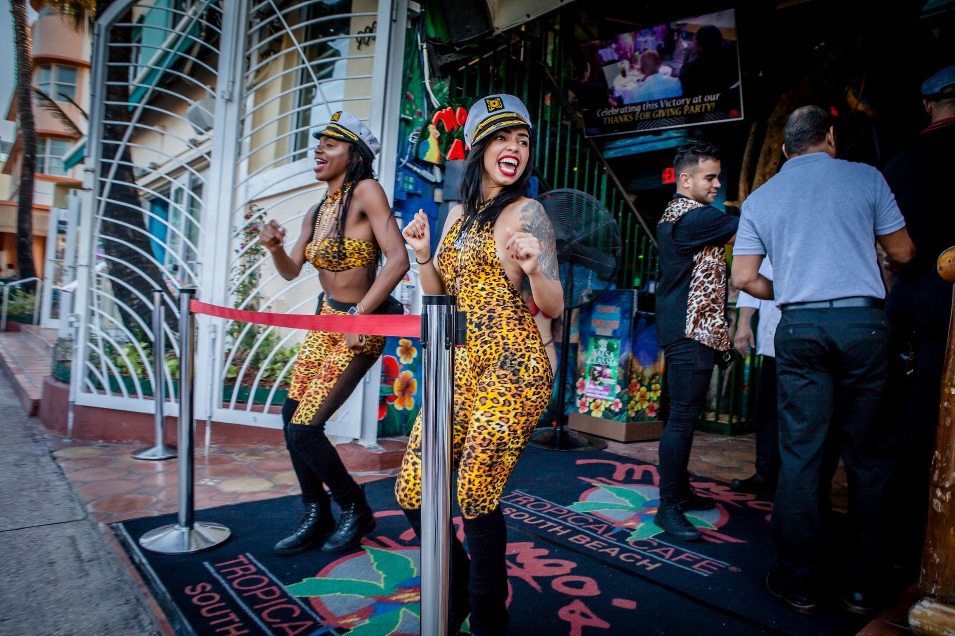 Two people in leopard-print outfits posing behind a red velvet rope at a colorful entrance