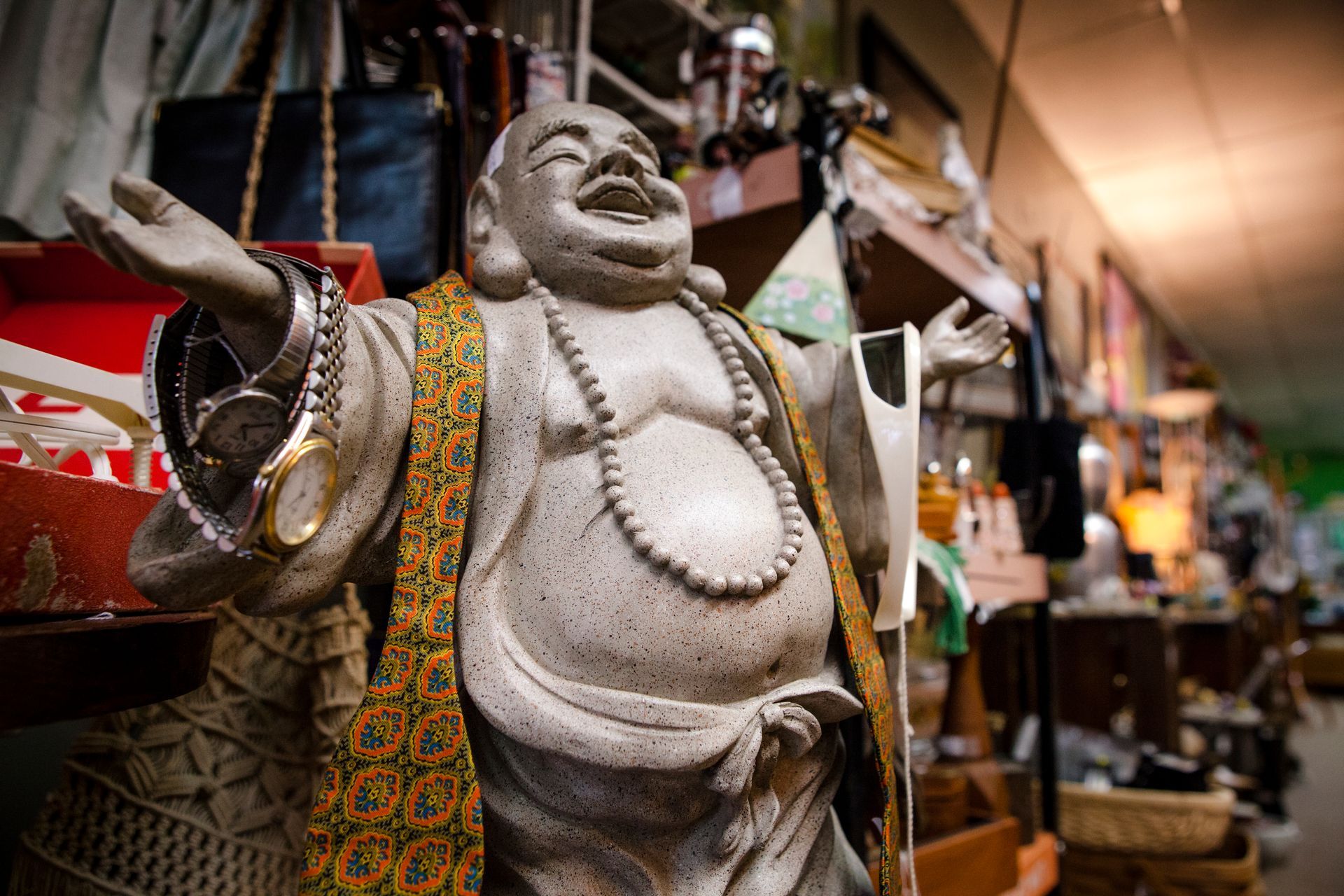 Stone Buddha statue with raised arm in a colorful market stall with hanging crafts and shelves