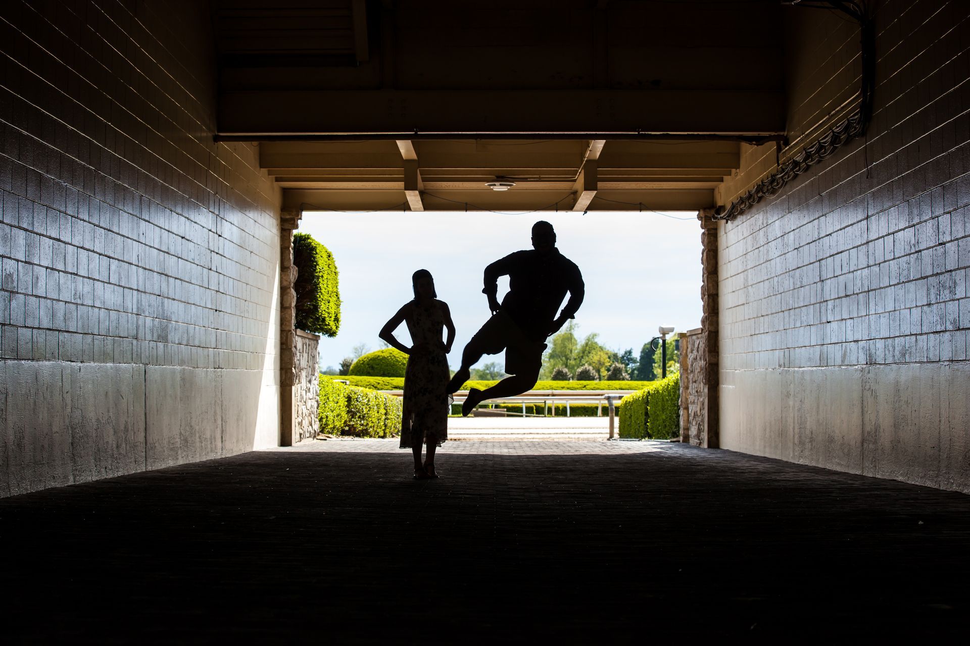 Two silhouetted people in a tunnel, one running and one jumping toward daylight outside.