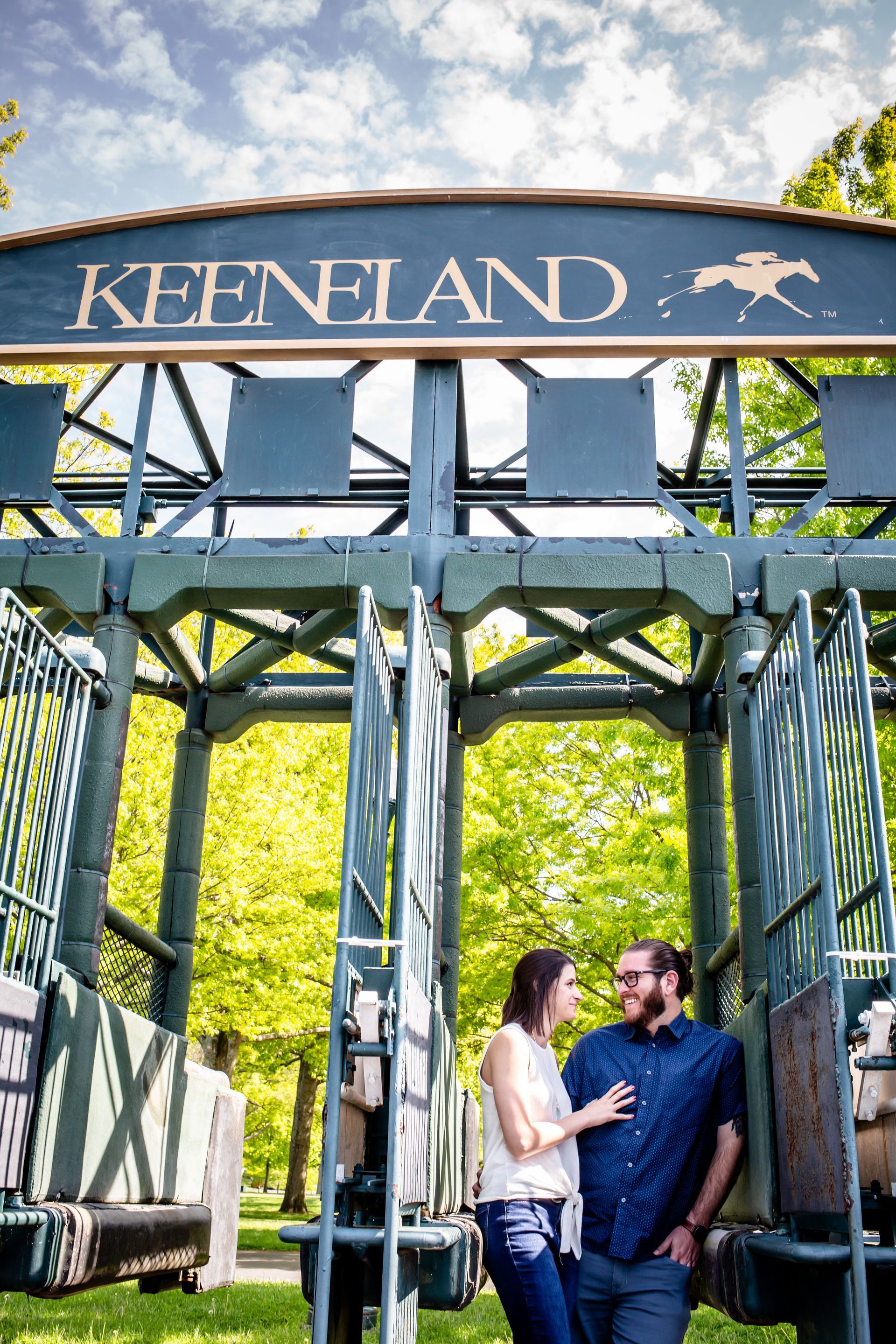 Couple standing beneath the Keeneland entrance arch on a sunny day