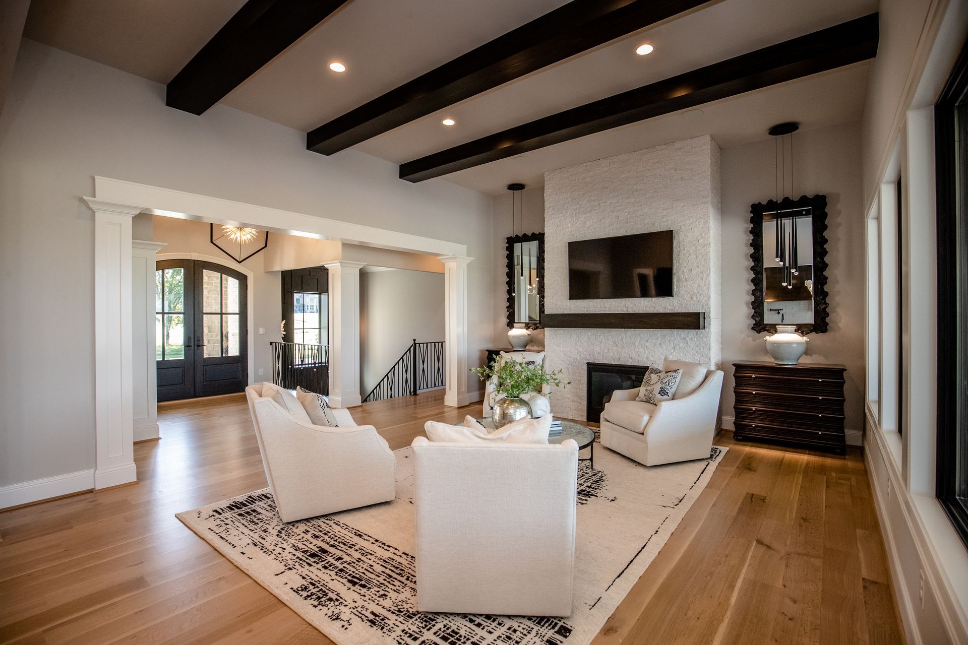 Bright modern living room with white sofas, wood floors, exposed beams, and a fireplace.