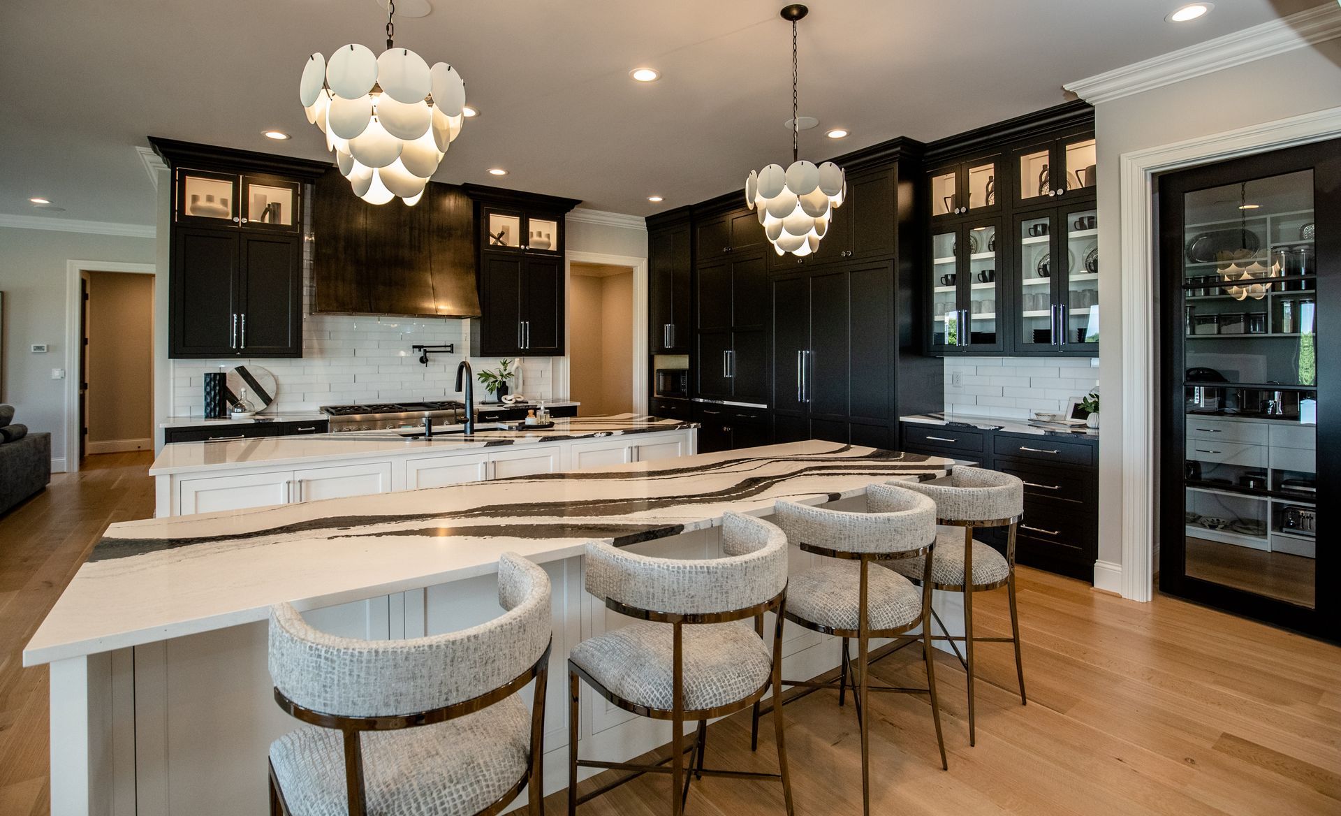 Modern black-and-white kitchen with marble island, tufted stools, pendant lights, and glass-front cabinets