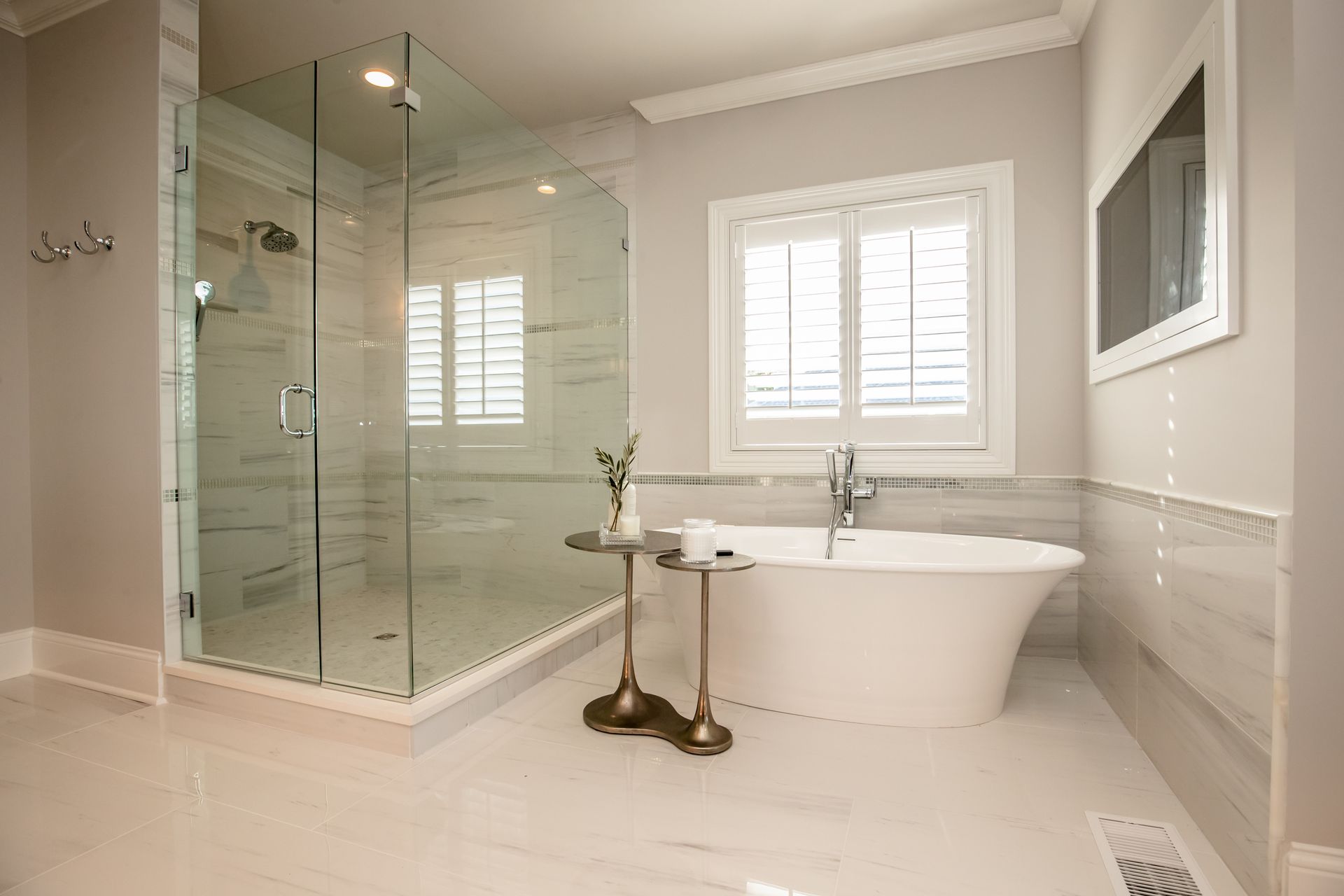 Bright modern bathroom with glass shower enclosure, freestanding tub, and white shutters
