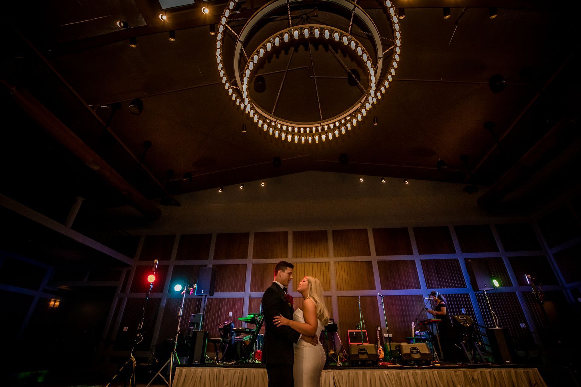 Couple slow dancing under a chandelier in a dimly lit banquet hall with purple lighting