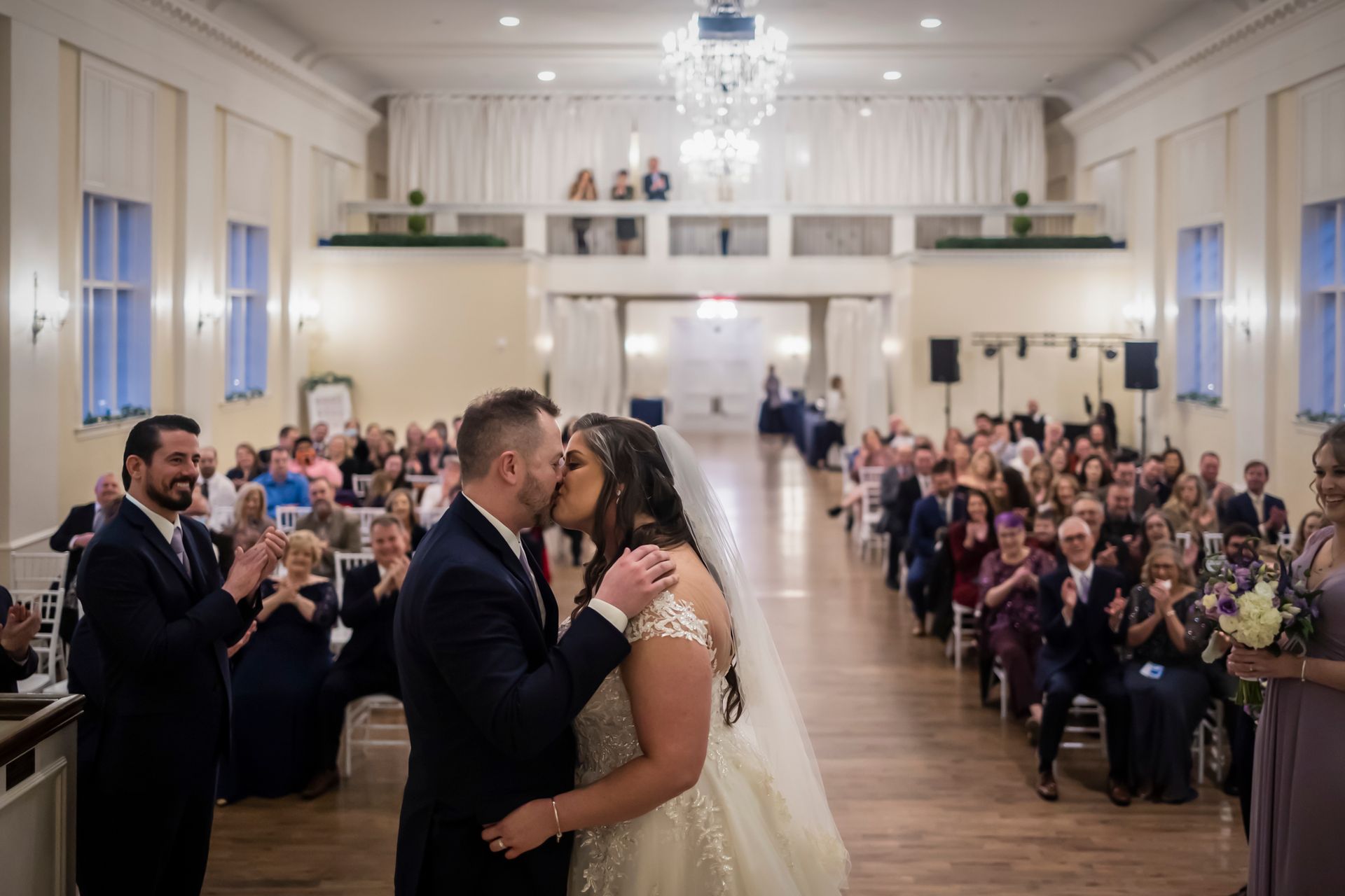 Bride and groom kissing in a bright church aisle during a wedding ceremony, guests seated on both sides