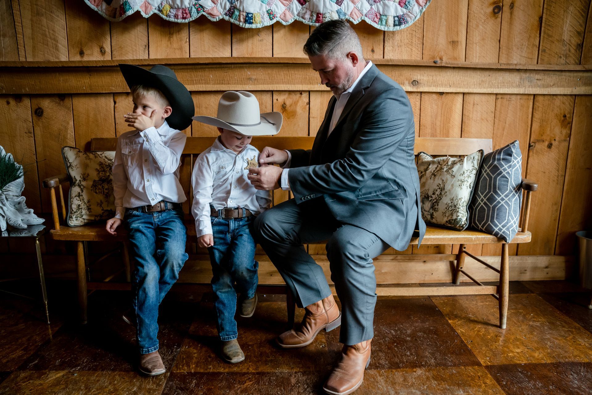 Man in suit and two children in cowboy hats seated on a bench in a rustic wooden room