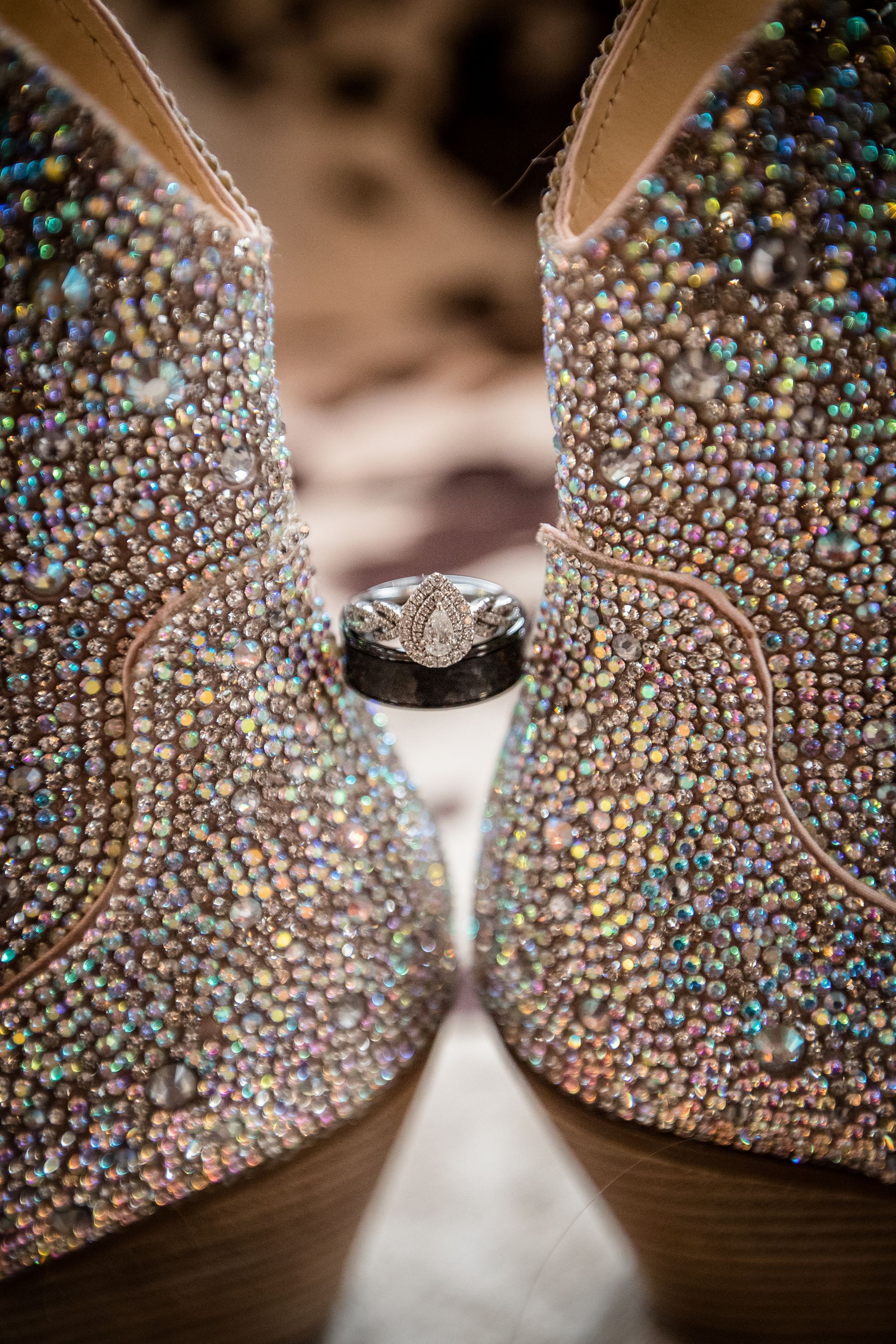 Sparkling rhinestone-covered shoes touching toe to toe, with a ring visible between them.