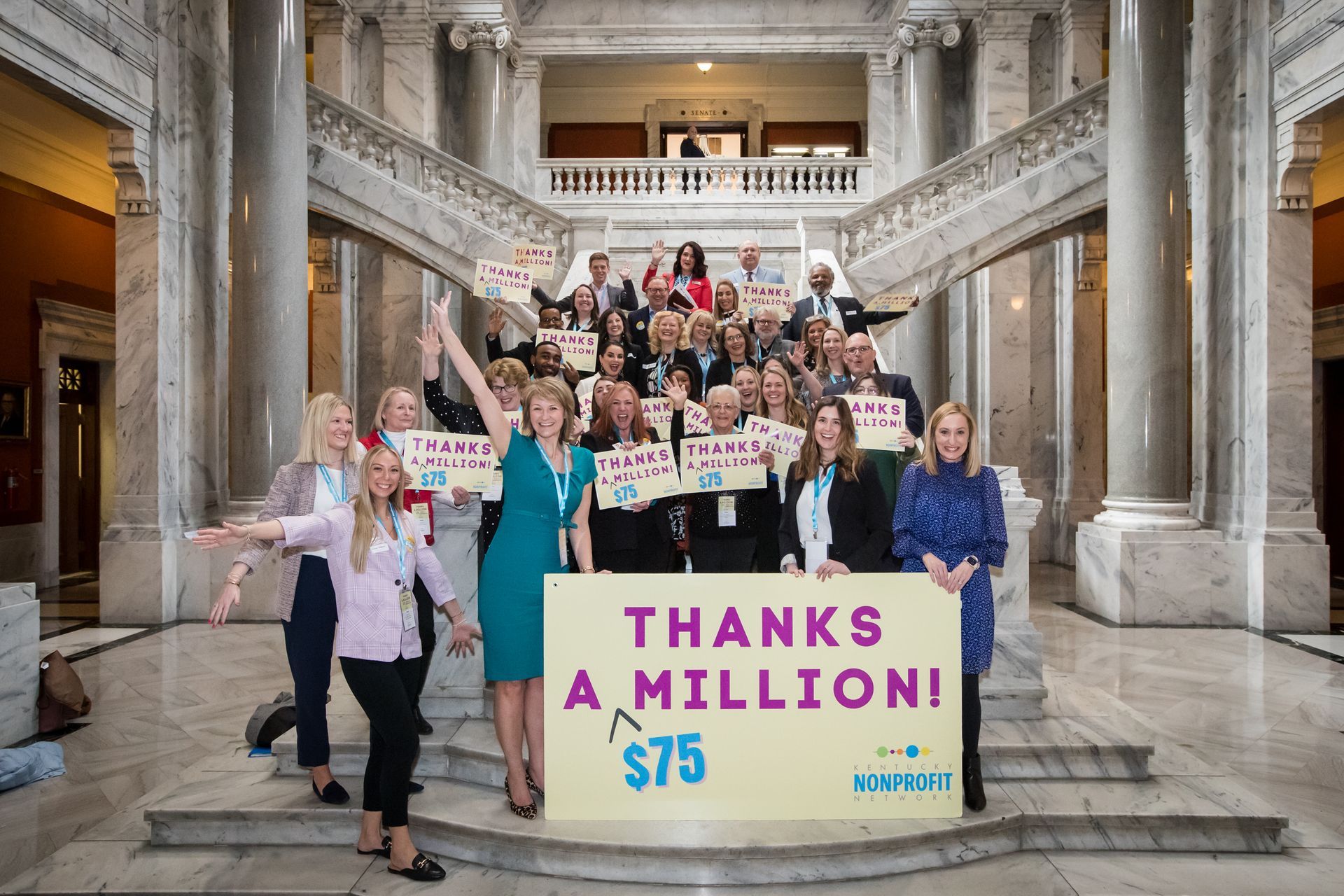 Group of people on grand staircase holding a sign reading “THANKS A MILLION! $75”