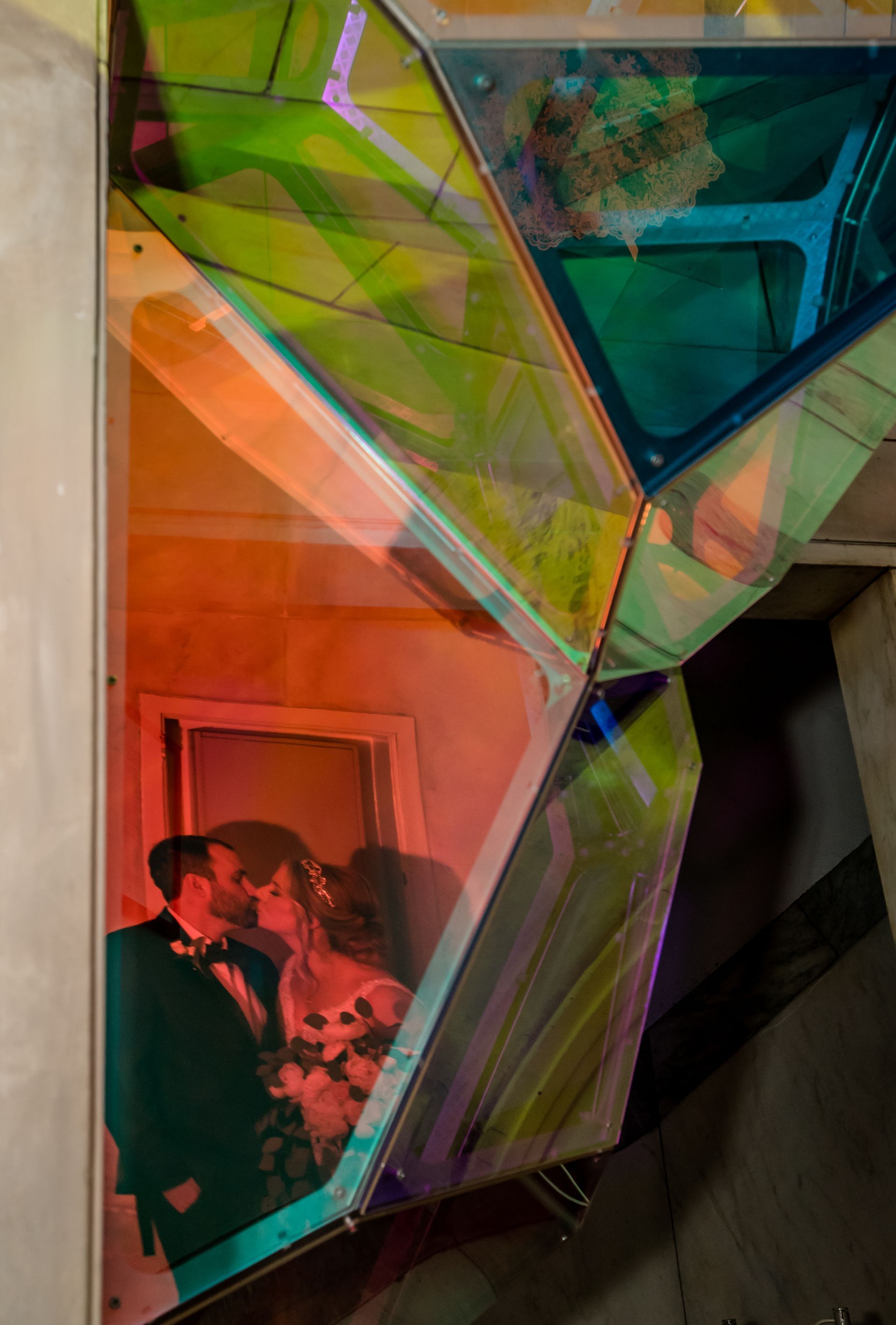 Abstract colorful geometric glass panels with a small red-lit portrait reflection in the lower left